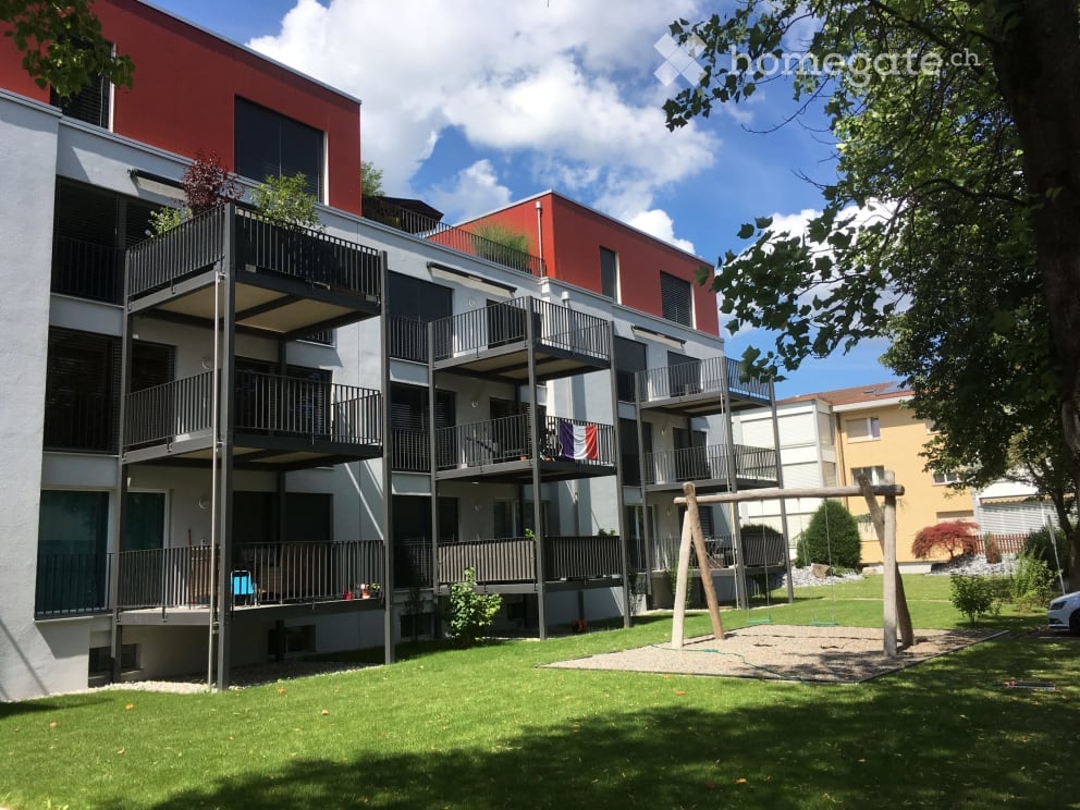 3 story apartment building, red and white exterior, multiple balconies, playground