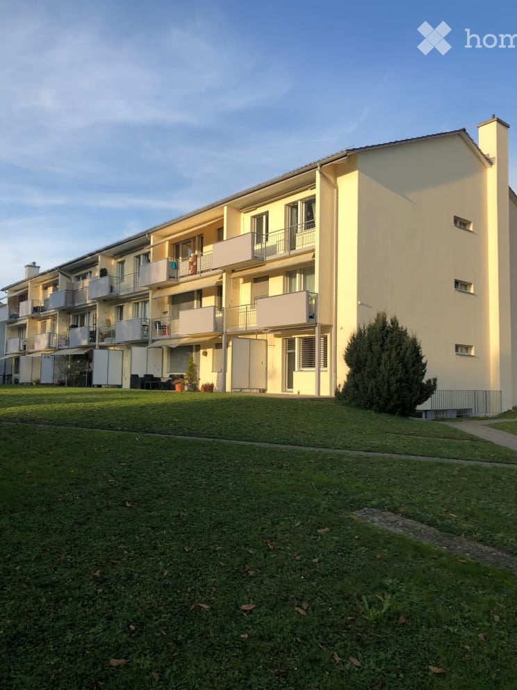 Multi-story residential building with multiple balconies and a well-maintained lawn in front.