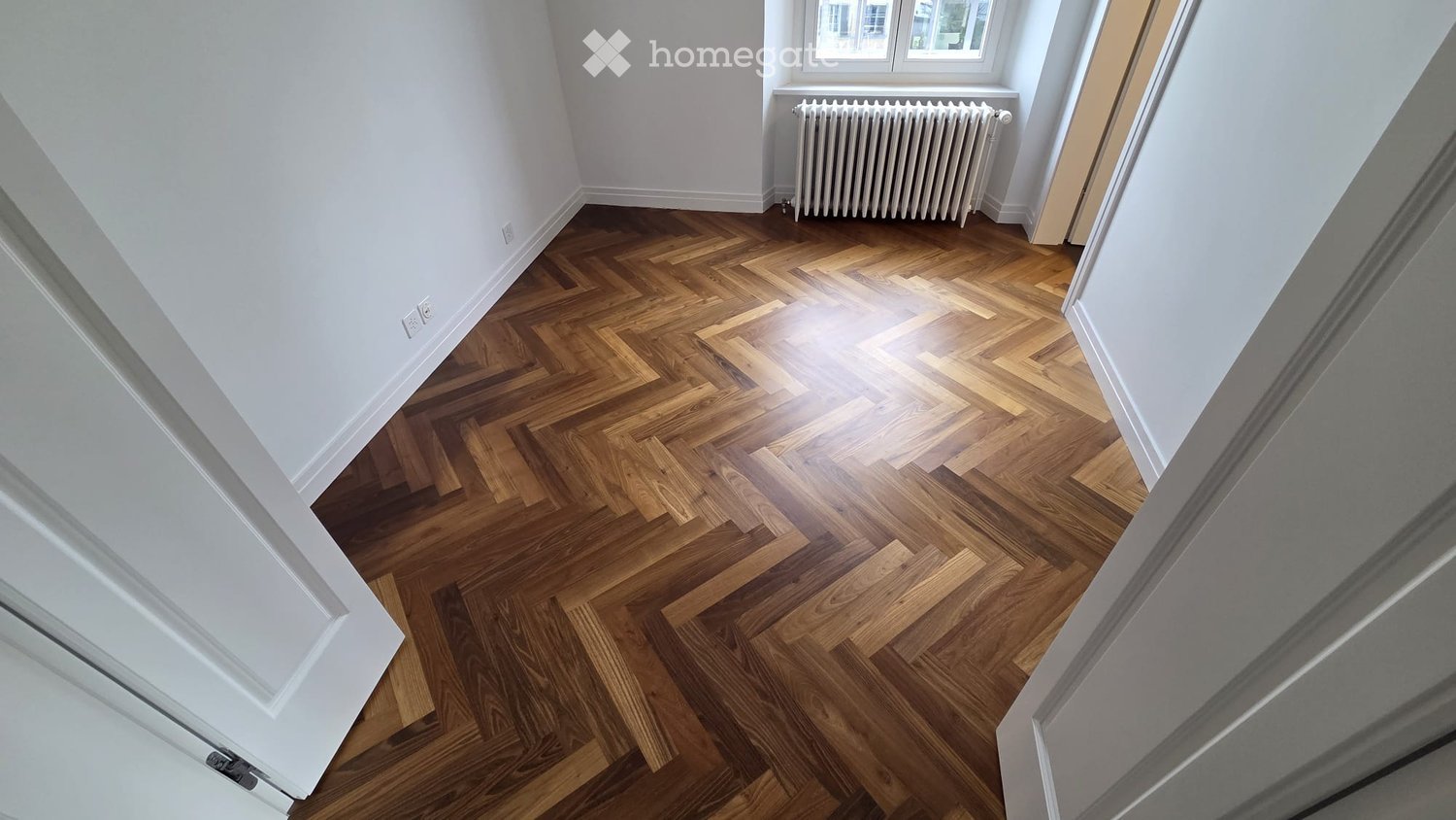 Completely empty room with bare walls and wooden herringbone floor. No furniture or equipment.
