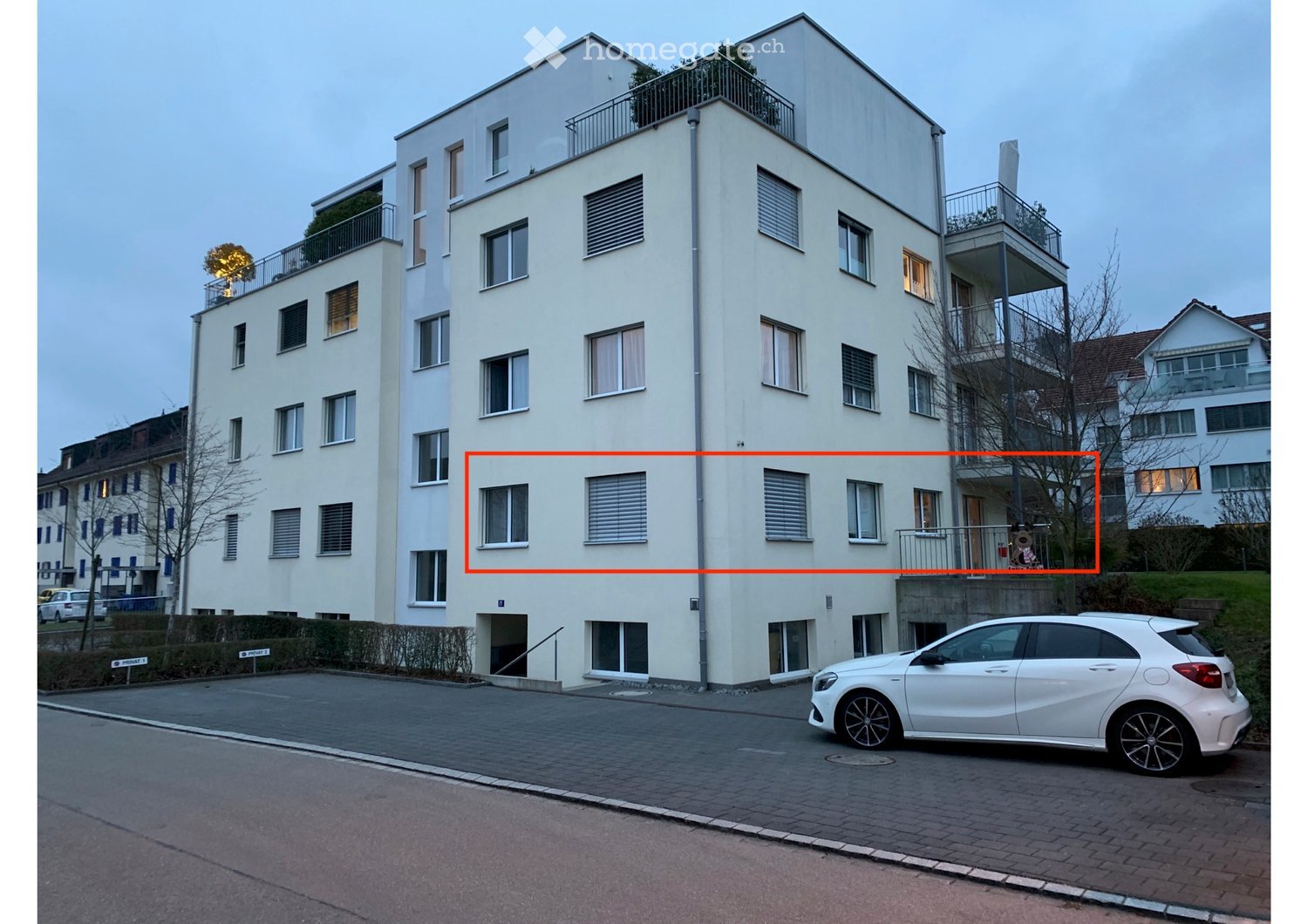 Modern multi-story residential building with white facade, multiple windows, balconies, and a parked car in front.