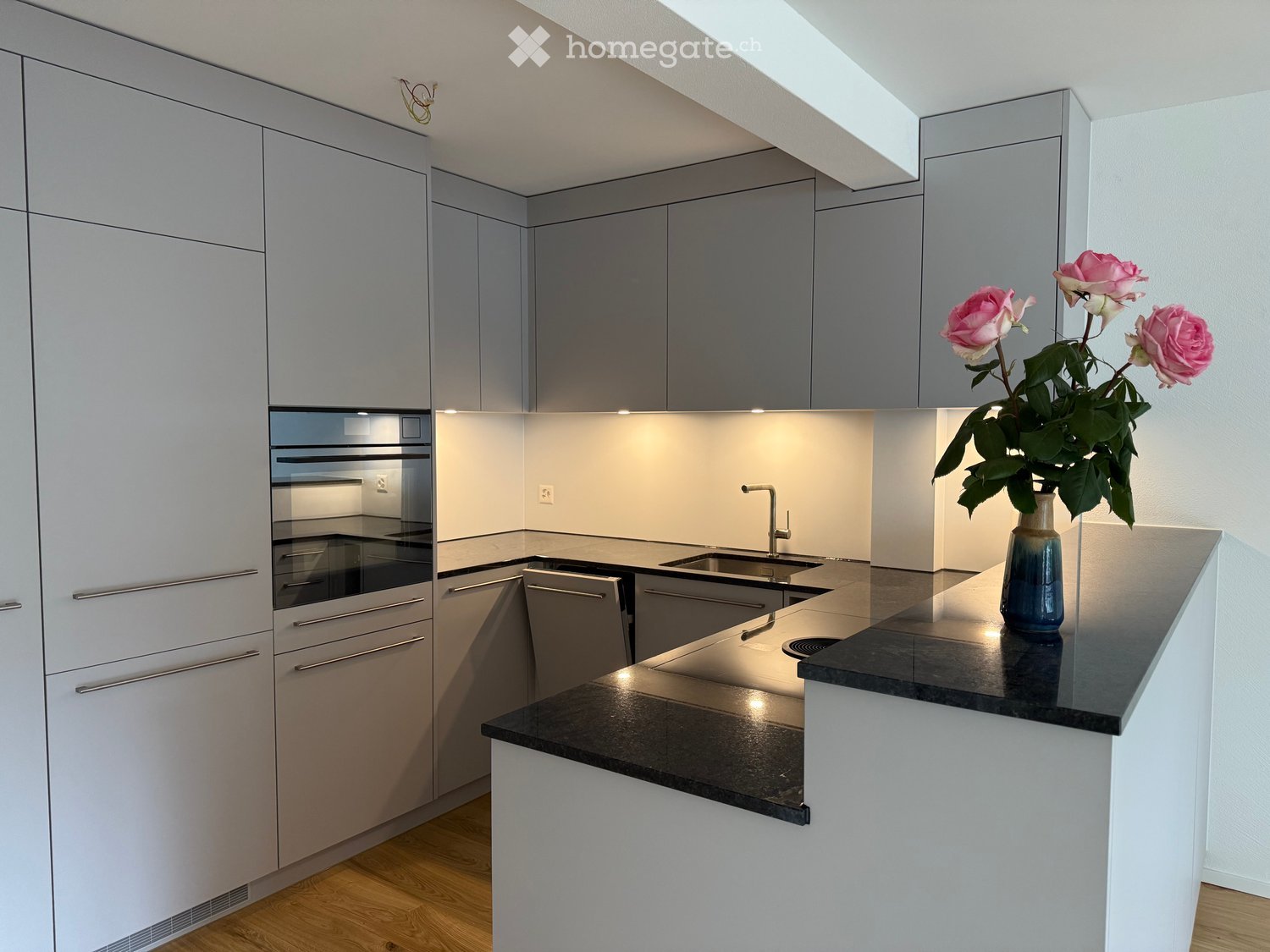 Modern kitchen with grey cabinets, stainless steel appliances, and a black countertop. A vase with pink roses is placed on the counter.