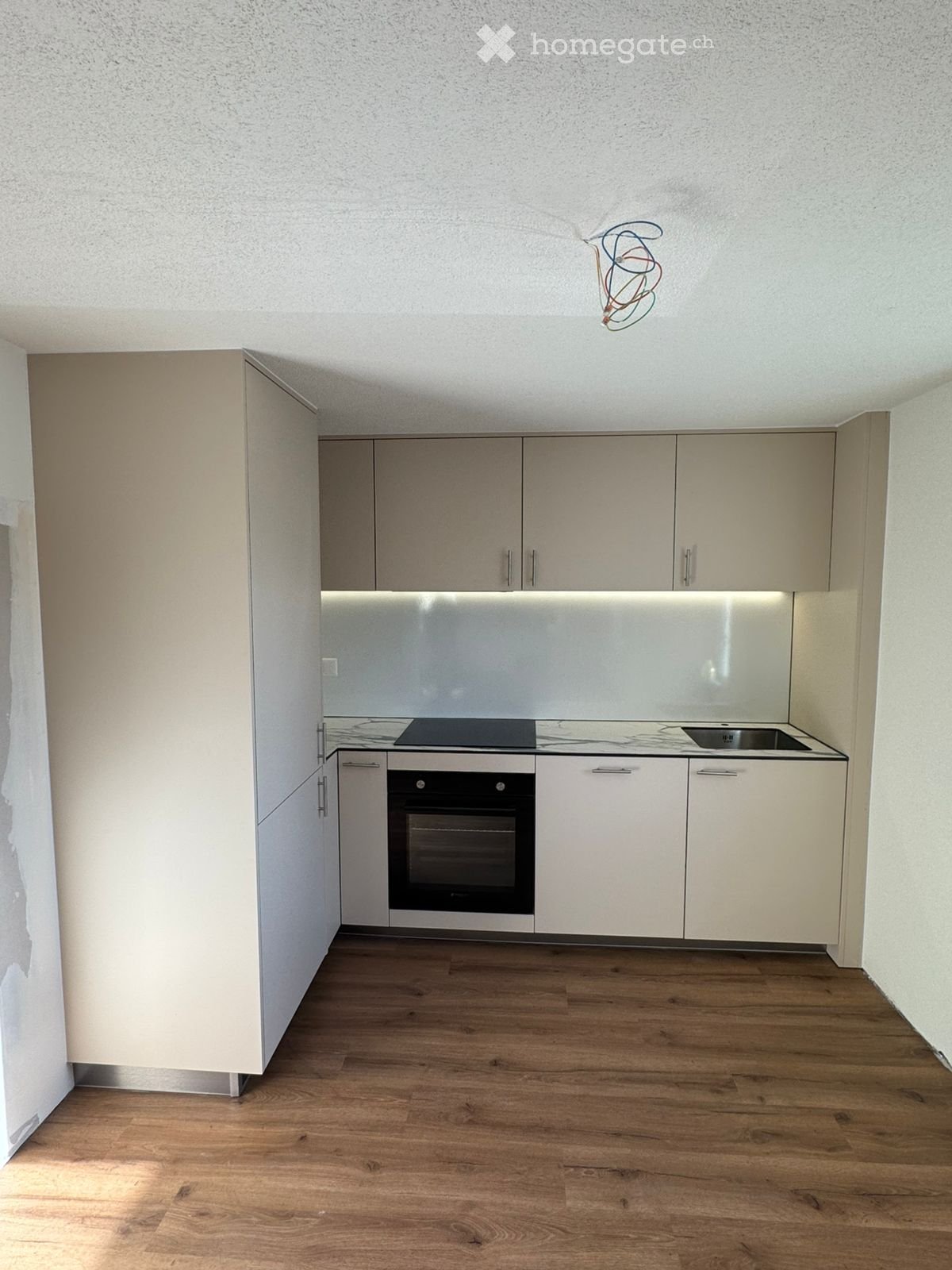 Modern kitchen with light-colored cabinets, a built-in oven, a sink, and a stove, featuring wooden flooring and a sleek design.