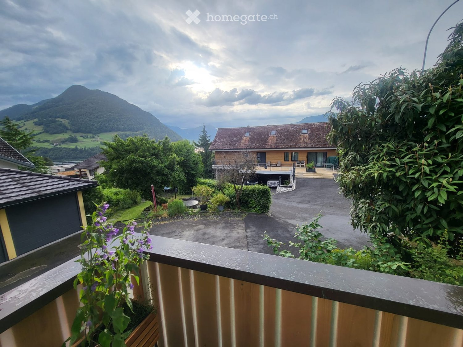 Balcony overlooking a scenic valley with a large house, garage, and surrounding greenery.