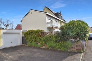Two-story house with a white garage, surrounded by greenery and a driveway.