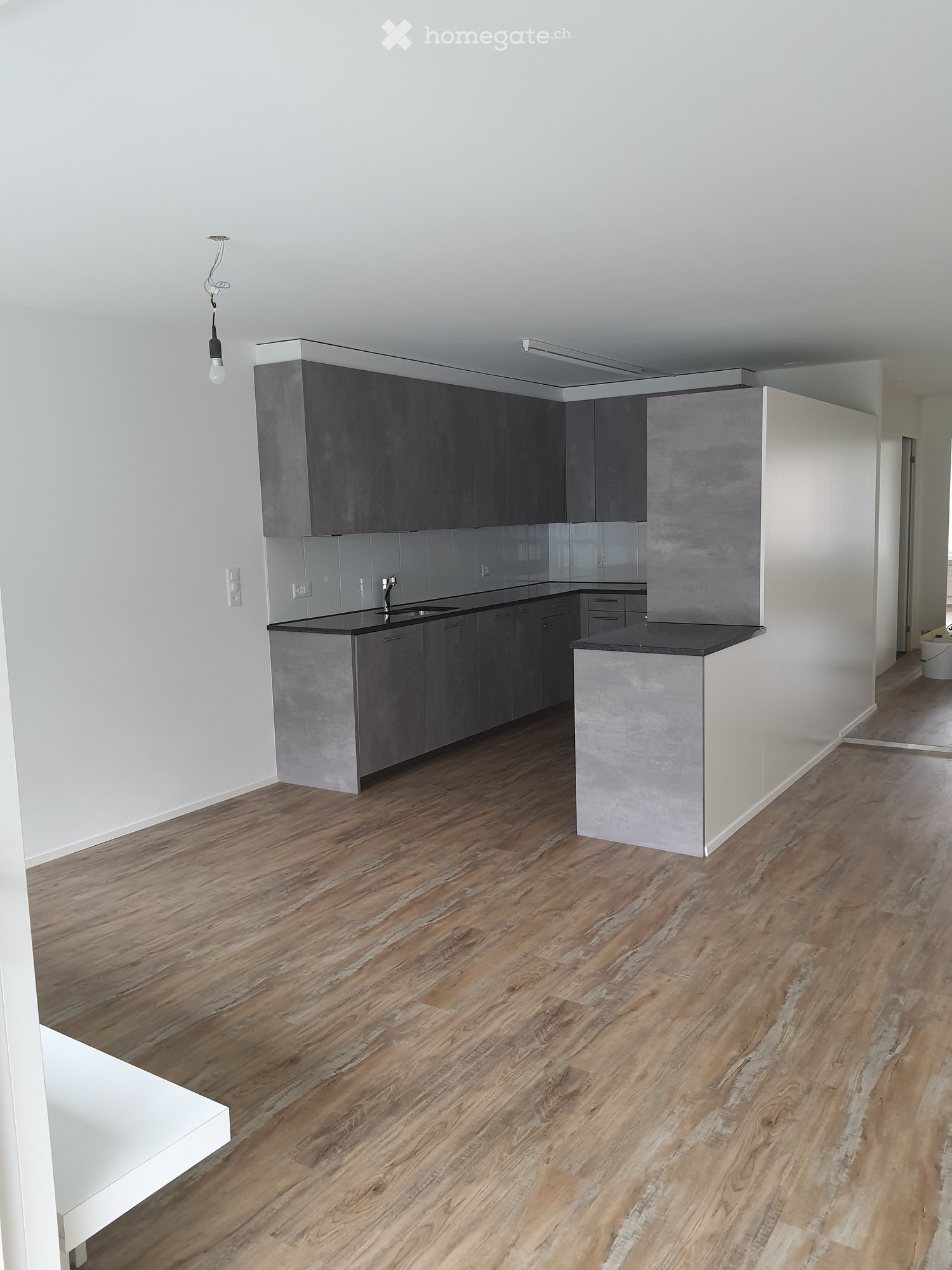 Modern kitchen with grey cabinets, black countertops, and wooden flooring.