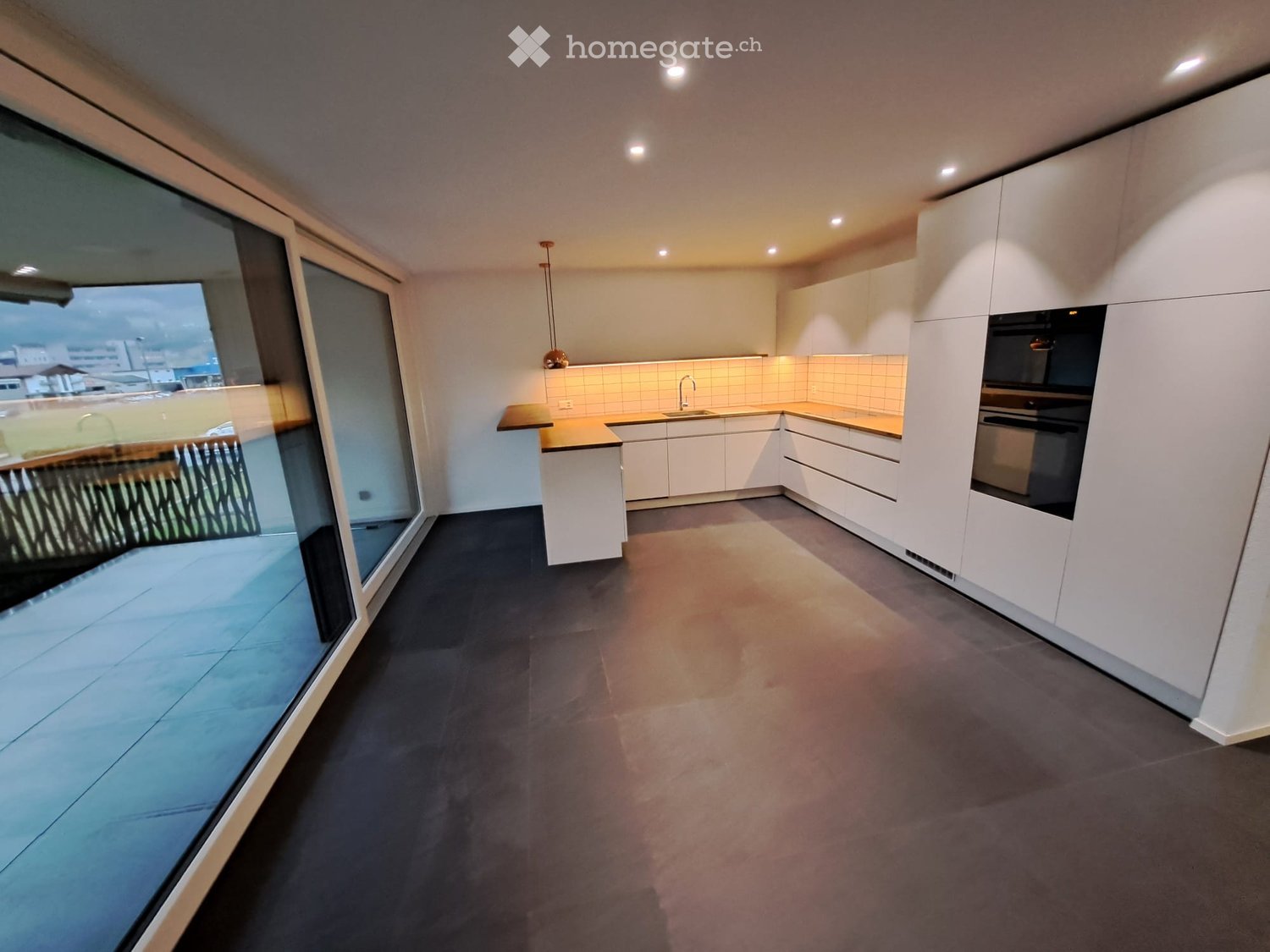 Modern kitchen with white cabinets, dark countertops, and a large window offering a view of the outdoor area.