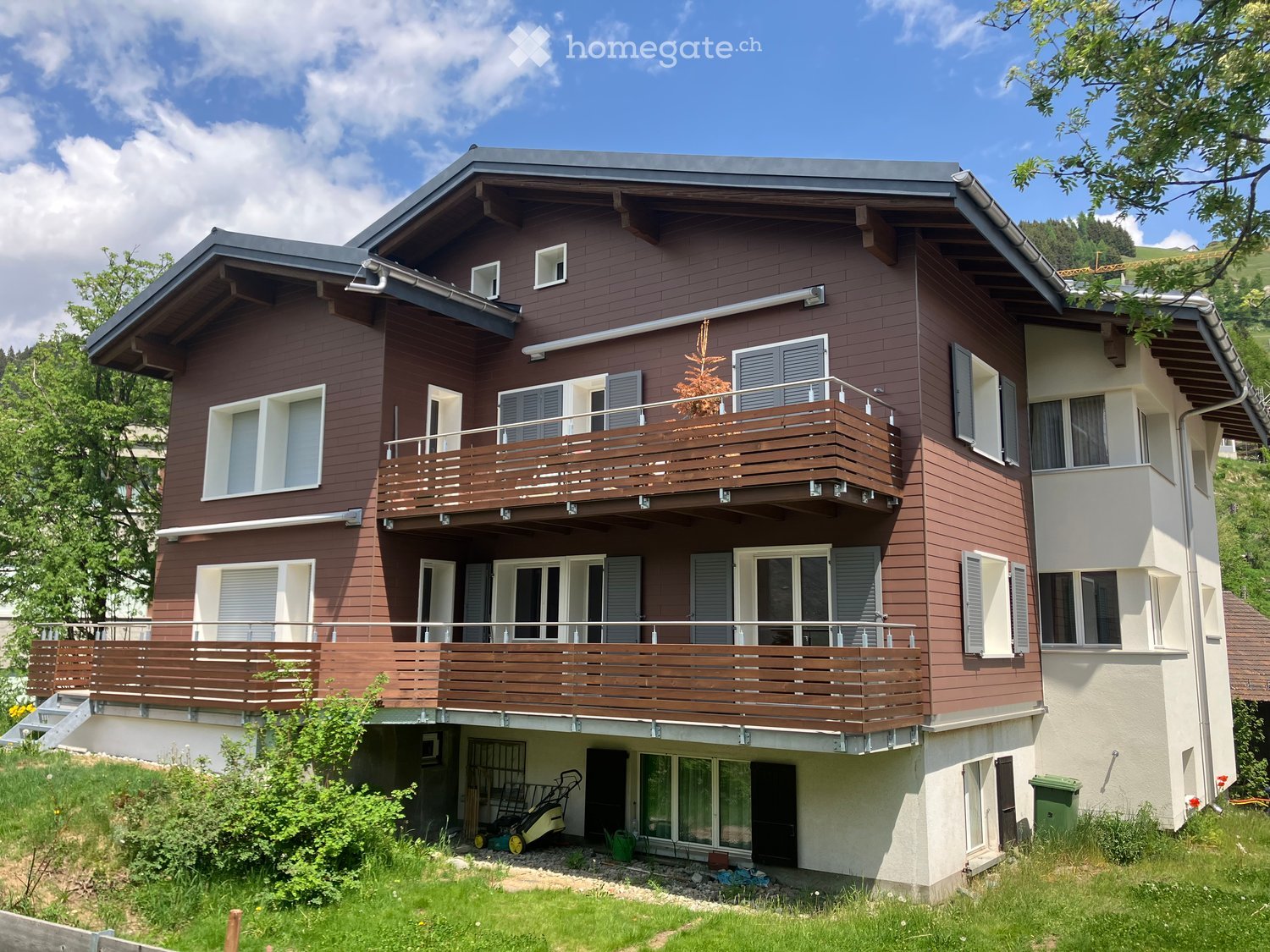 Two-story house with brown wooden siding, white trim, multiple windows, and balconies on both levels.