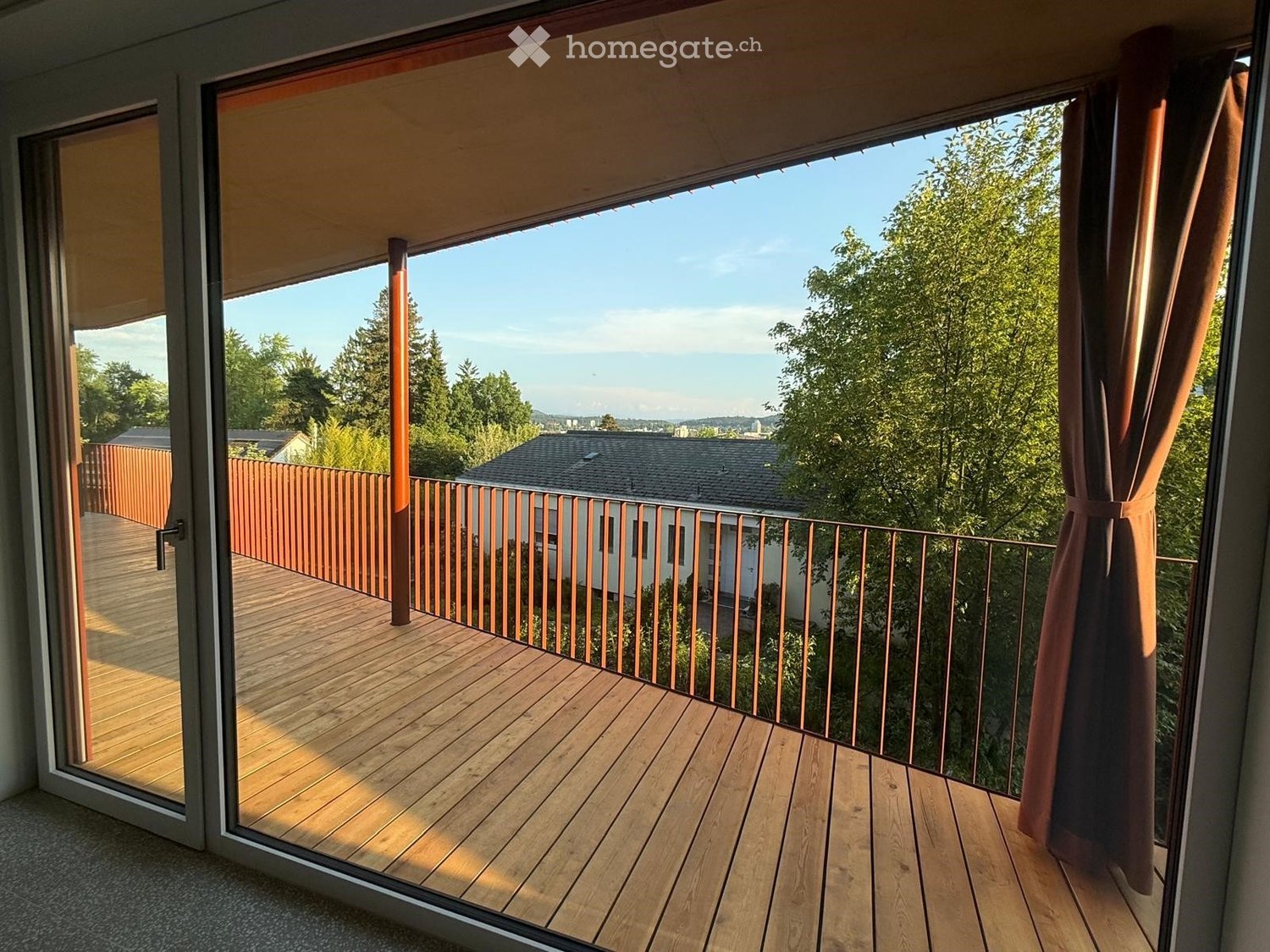 Balcony with wooden decking, metal railing, and sliding glass doors leading to the interior.