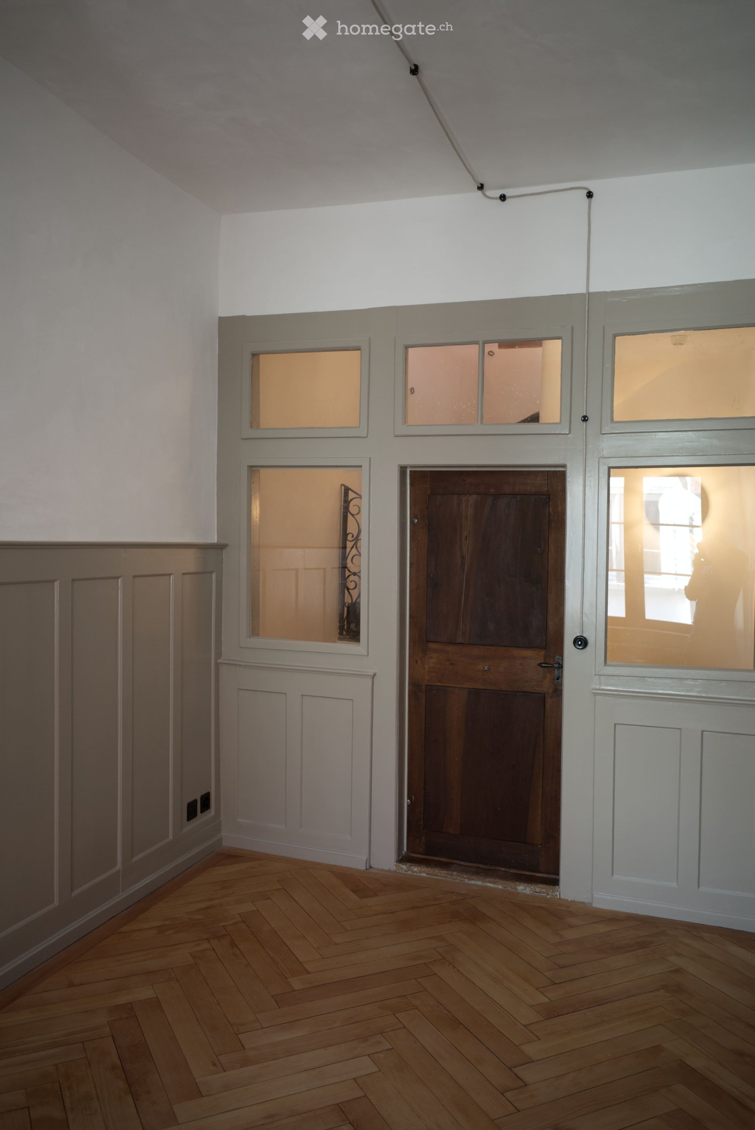 Empty room with wooden herringbone flooring, white walls, and multiple doors with frosted glass panels.