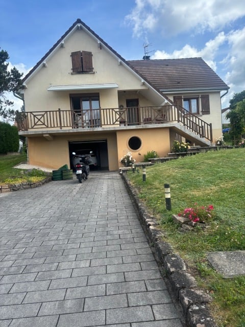 Two-story house with beige exterior, garage, raised ground floor, and balcony overlooking the front yard.