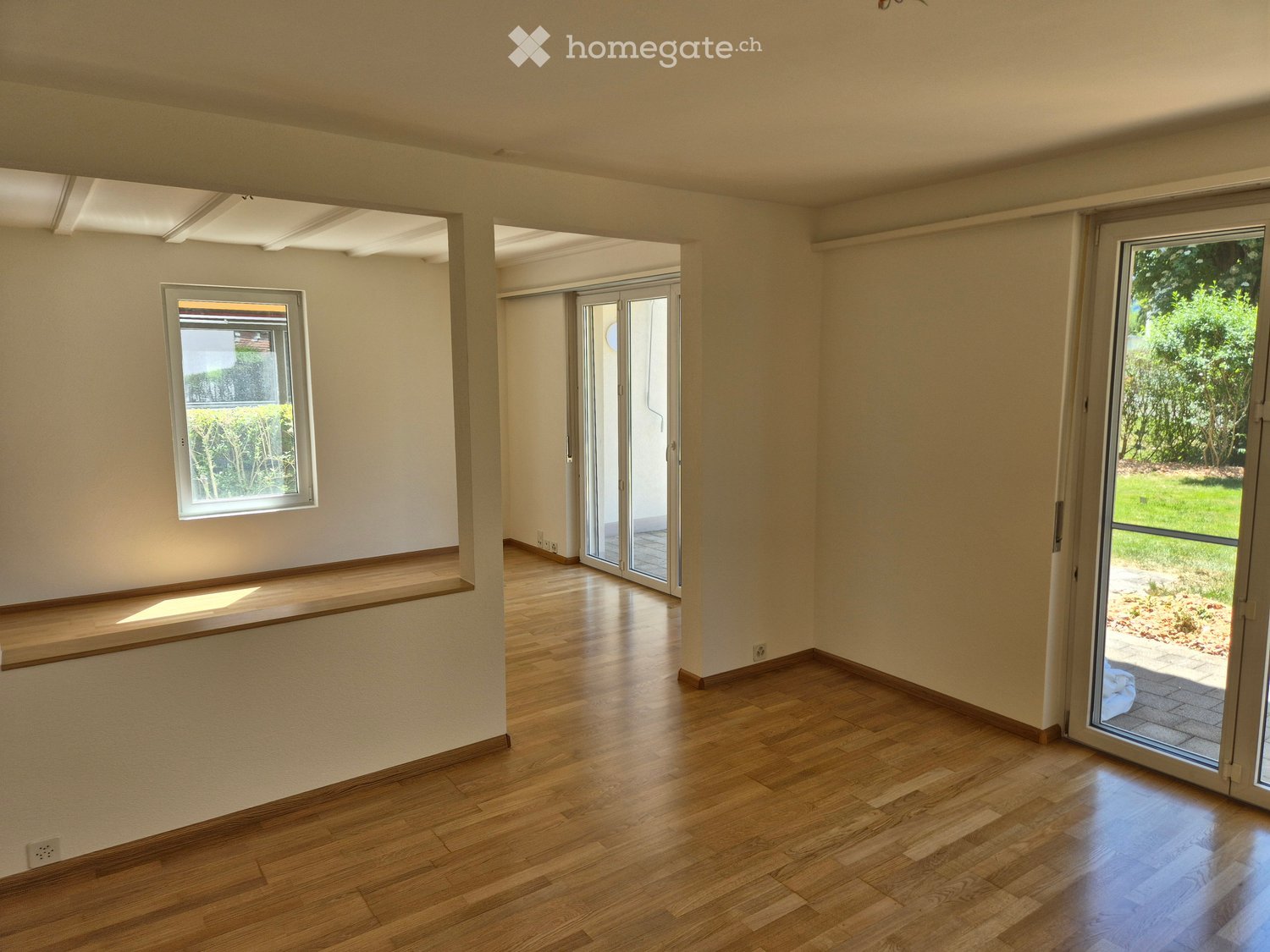 Empty room with wooden flooring, white walls, large windows, and sliding glass doors leading to an outdoor area.