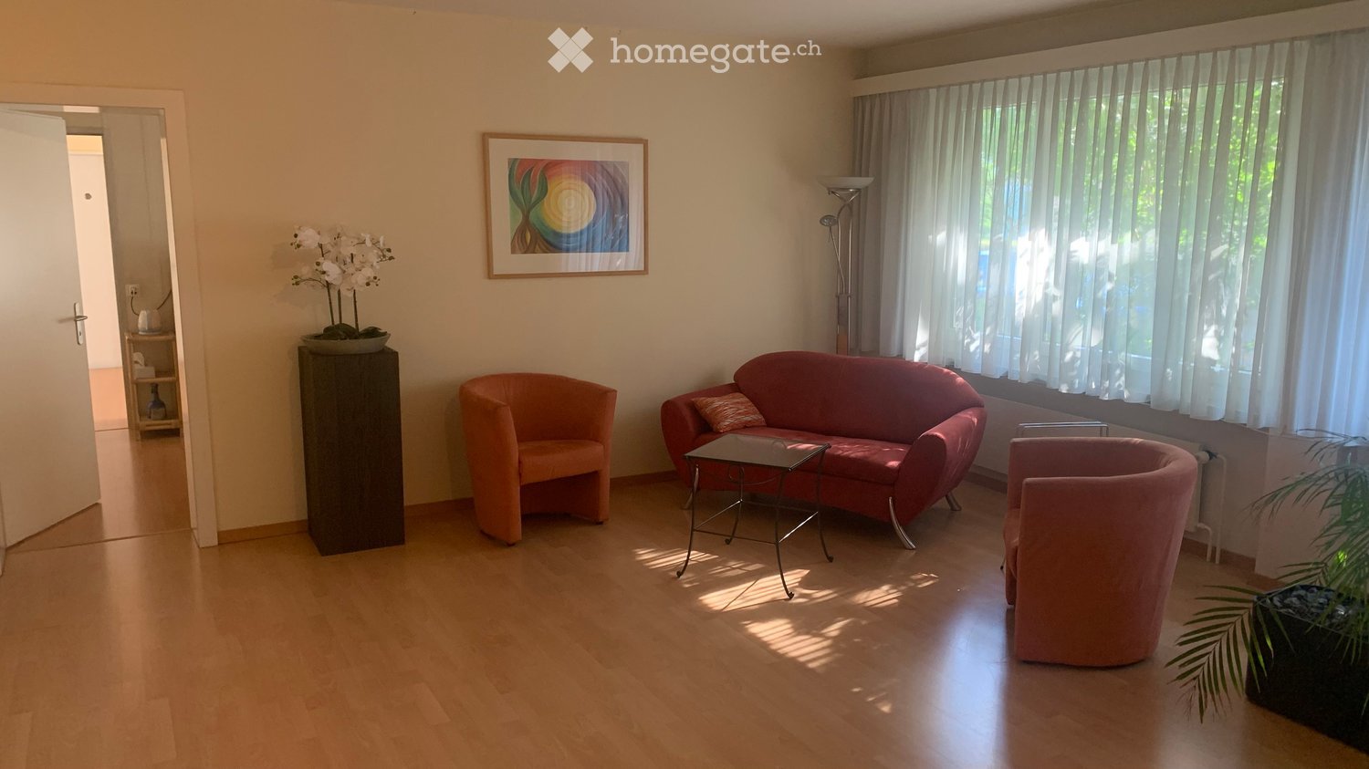 Wooden floor, red couch, two orange armchairs, coffee table, floor lamp, picture frame, curtains, plants