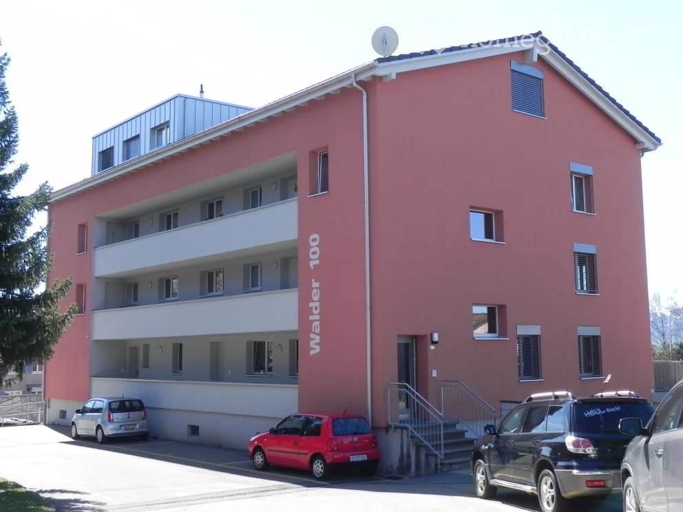 3 story building, pink exterior, white windows, multiple balconies, cars parked in front