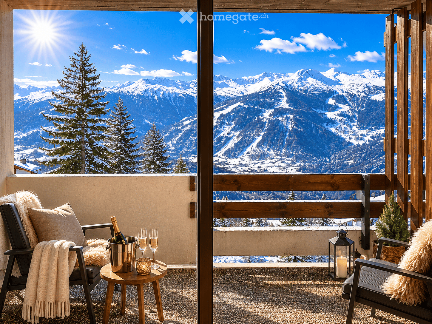 Balcony with two chairs, a small table holding a champagne bucket, glasses, and candles, overlooking snow-capped mountains and a clear blue sky.