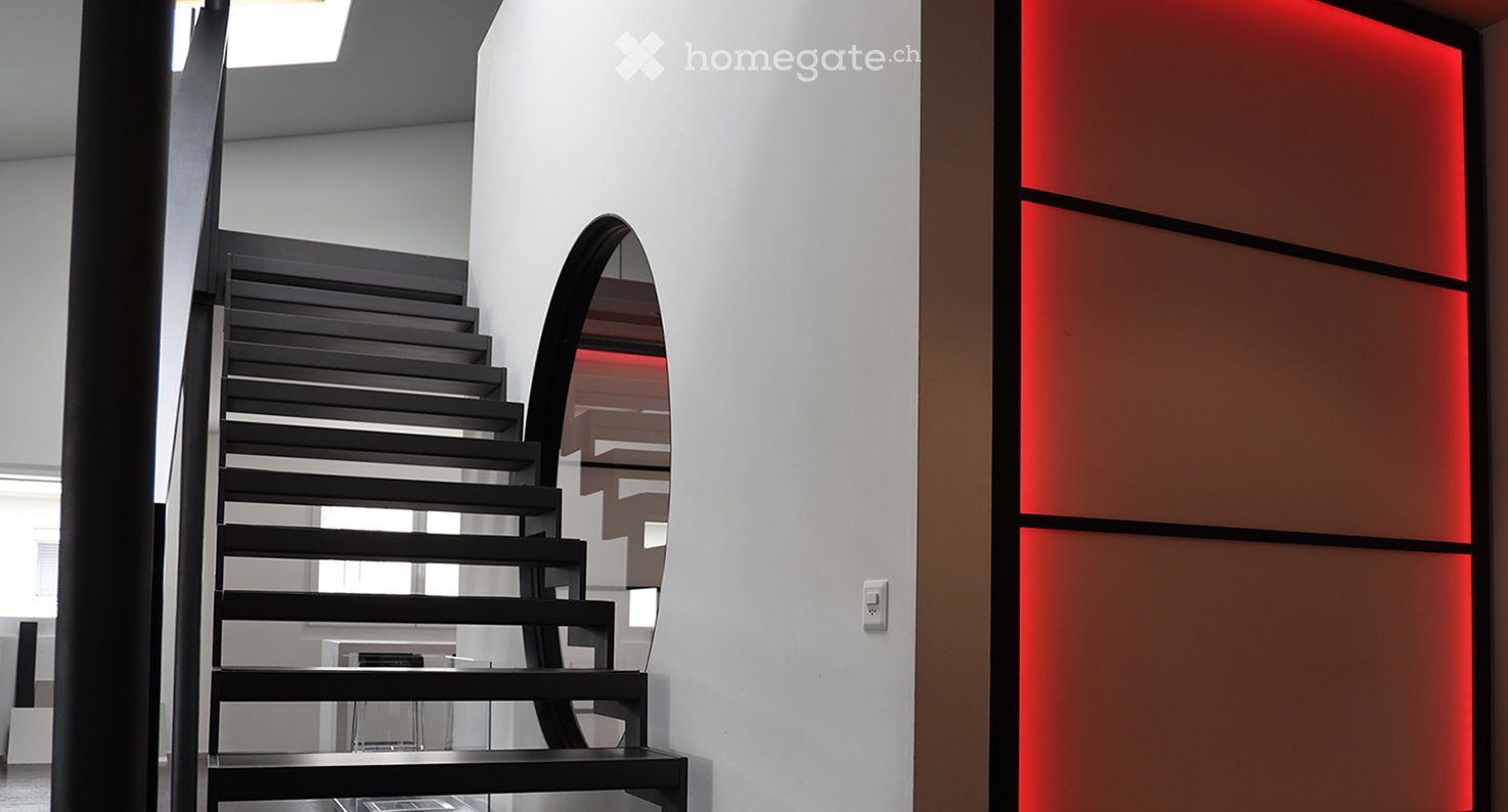 Modern hallway with a sleek black staircase, illuminated red wall panel, and a large mirror reflecting the staircase.
