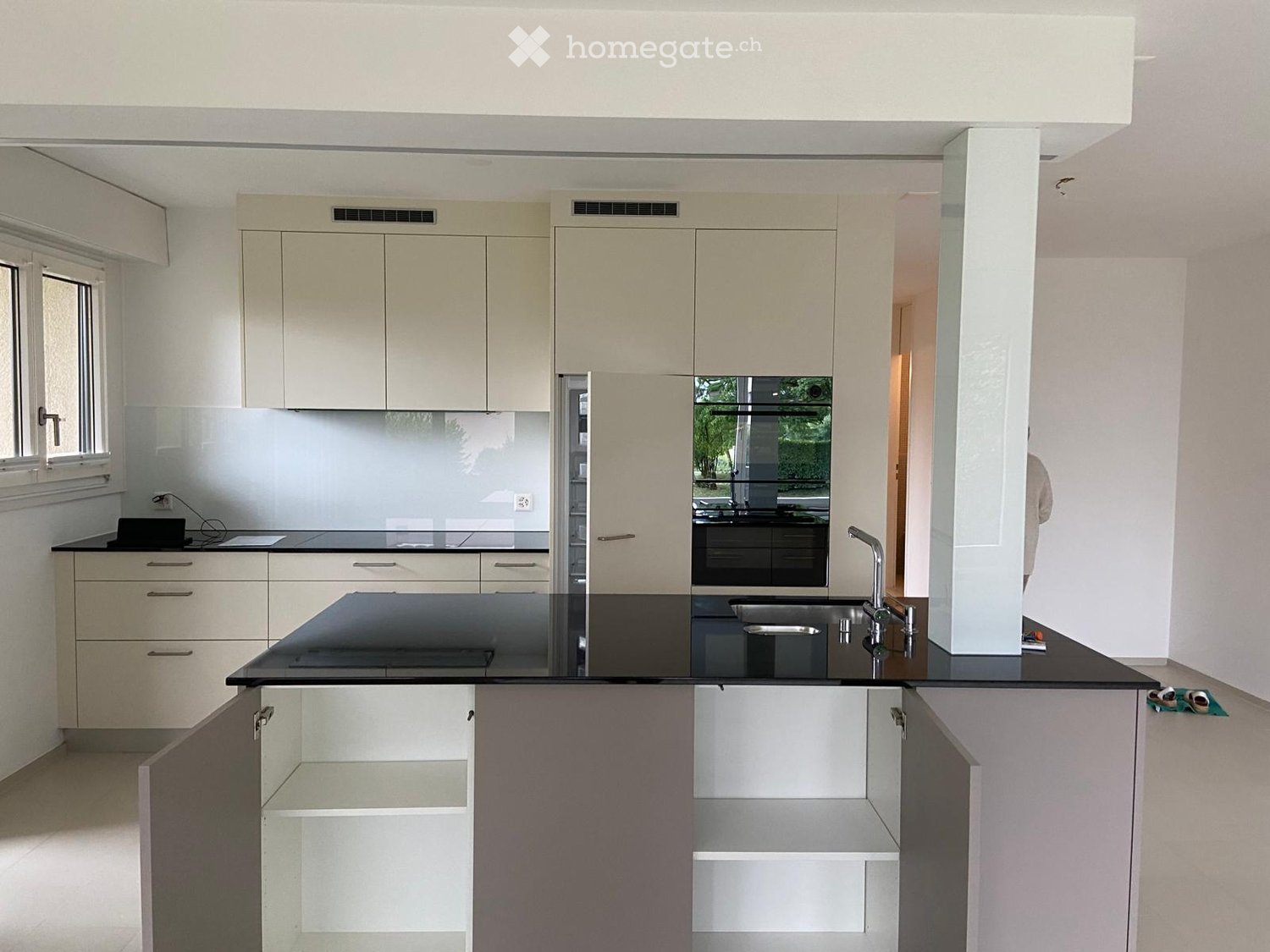 Modern kitchen with light-colored cabinets, black countertop, stainless steel sink, and a central island with open shelving.