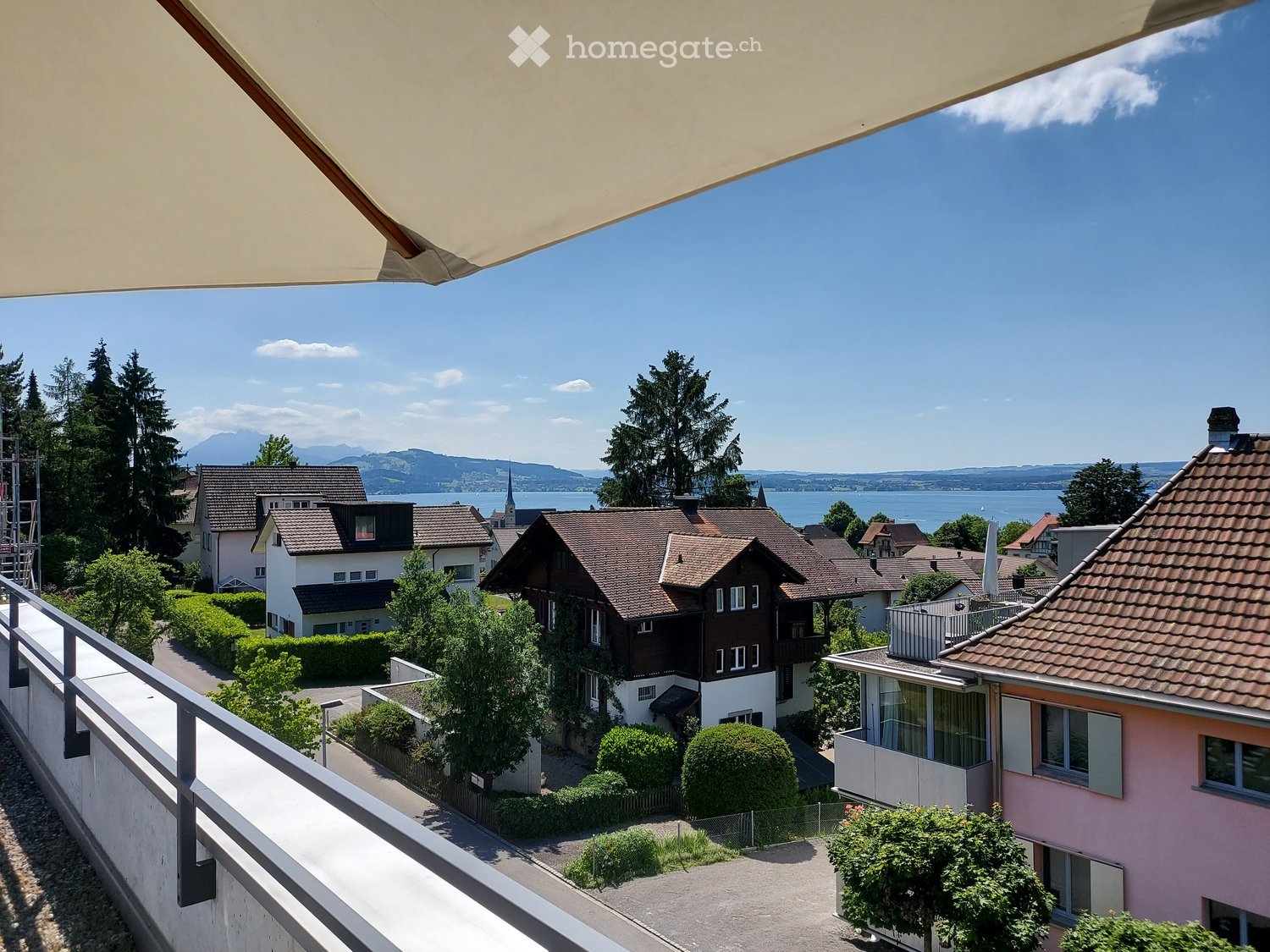 Balcony overlooking a residential area with houses, trees, and a distant lake and mountains.