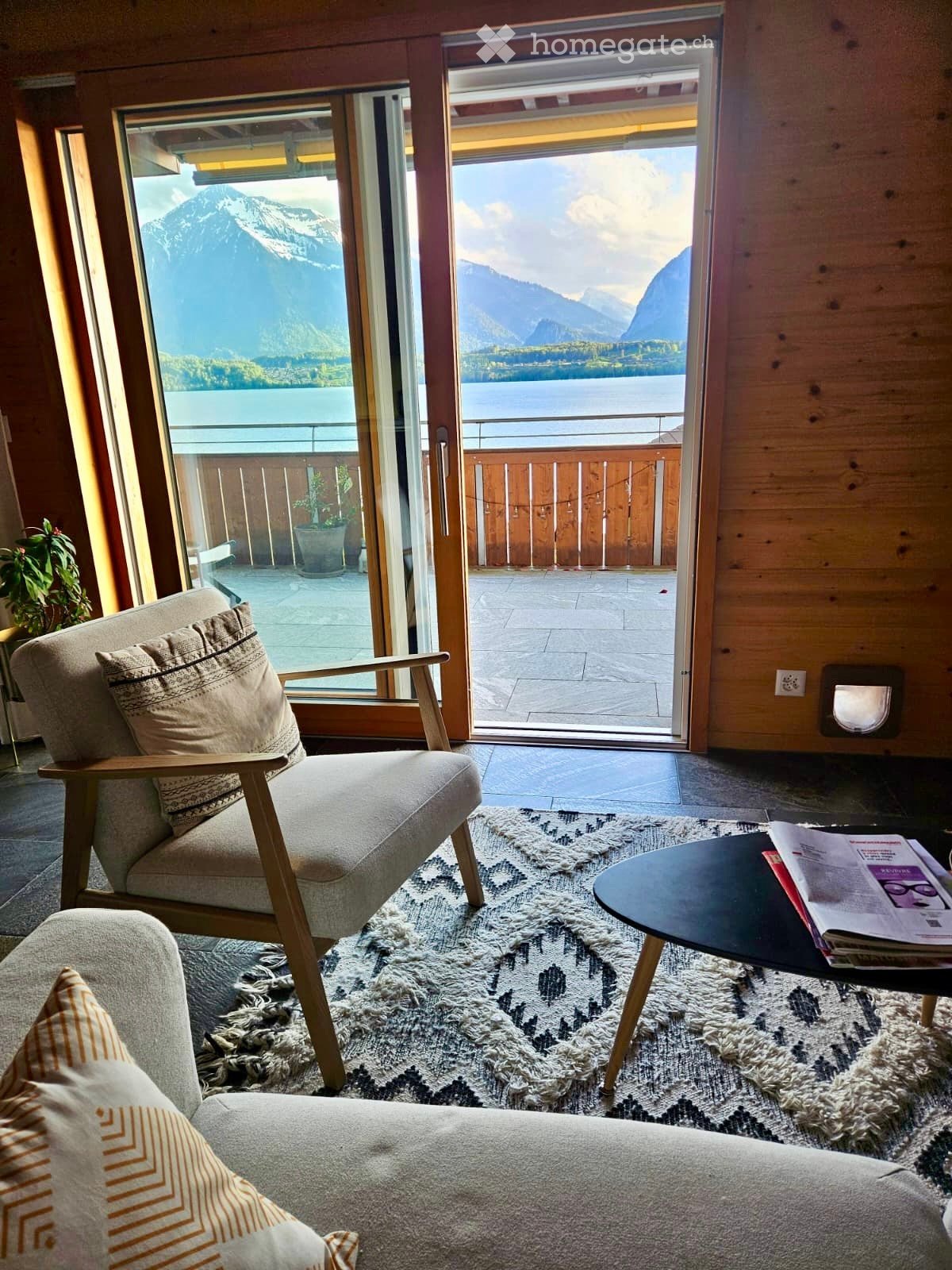 A cozy living room with a sofa, armchair, coffee table, and a view of mountains through large glass doors.