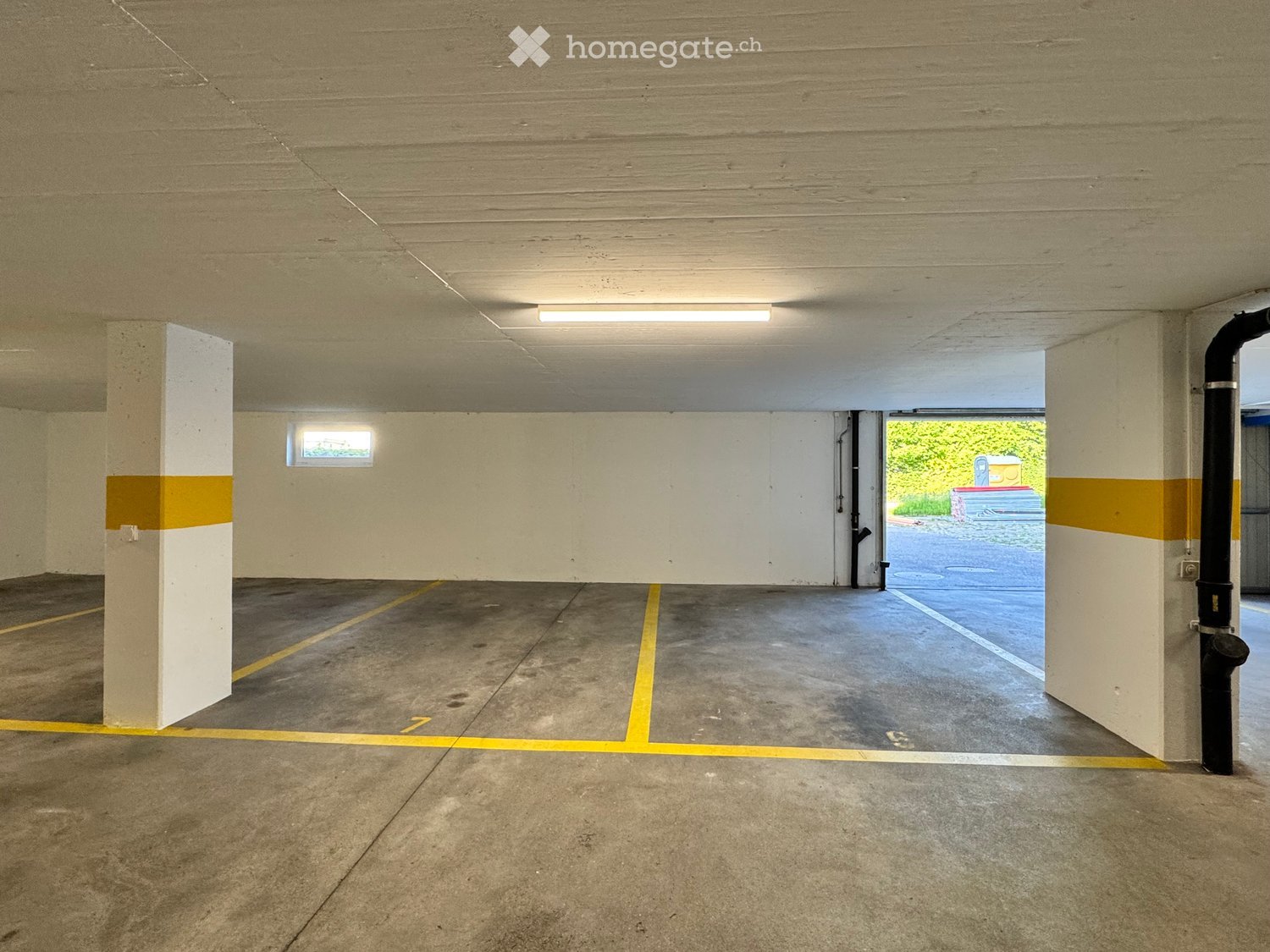 Underground parking area with concrete pillars, marked parking spaces, and a small window letting in natural light.