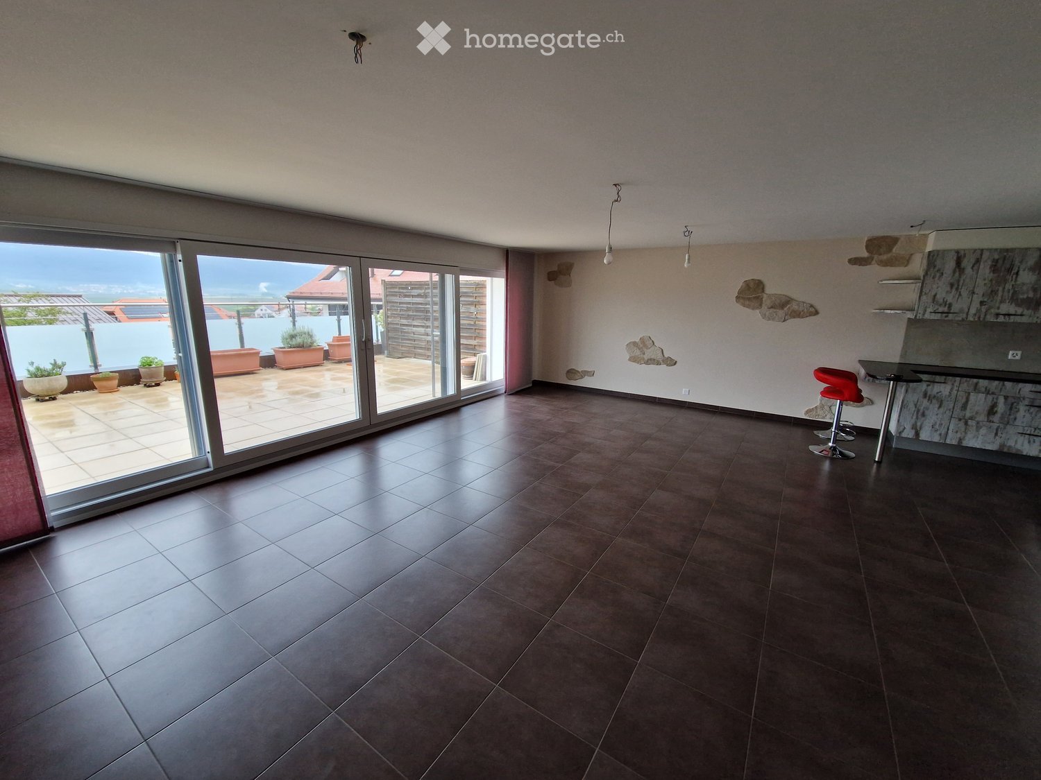 Open-plan space with tiled flooring, large sliding glass doors leading to a patio, and a small seating area with a table and stools.