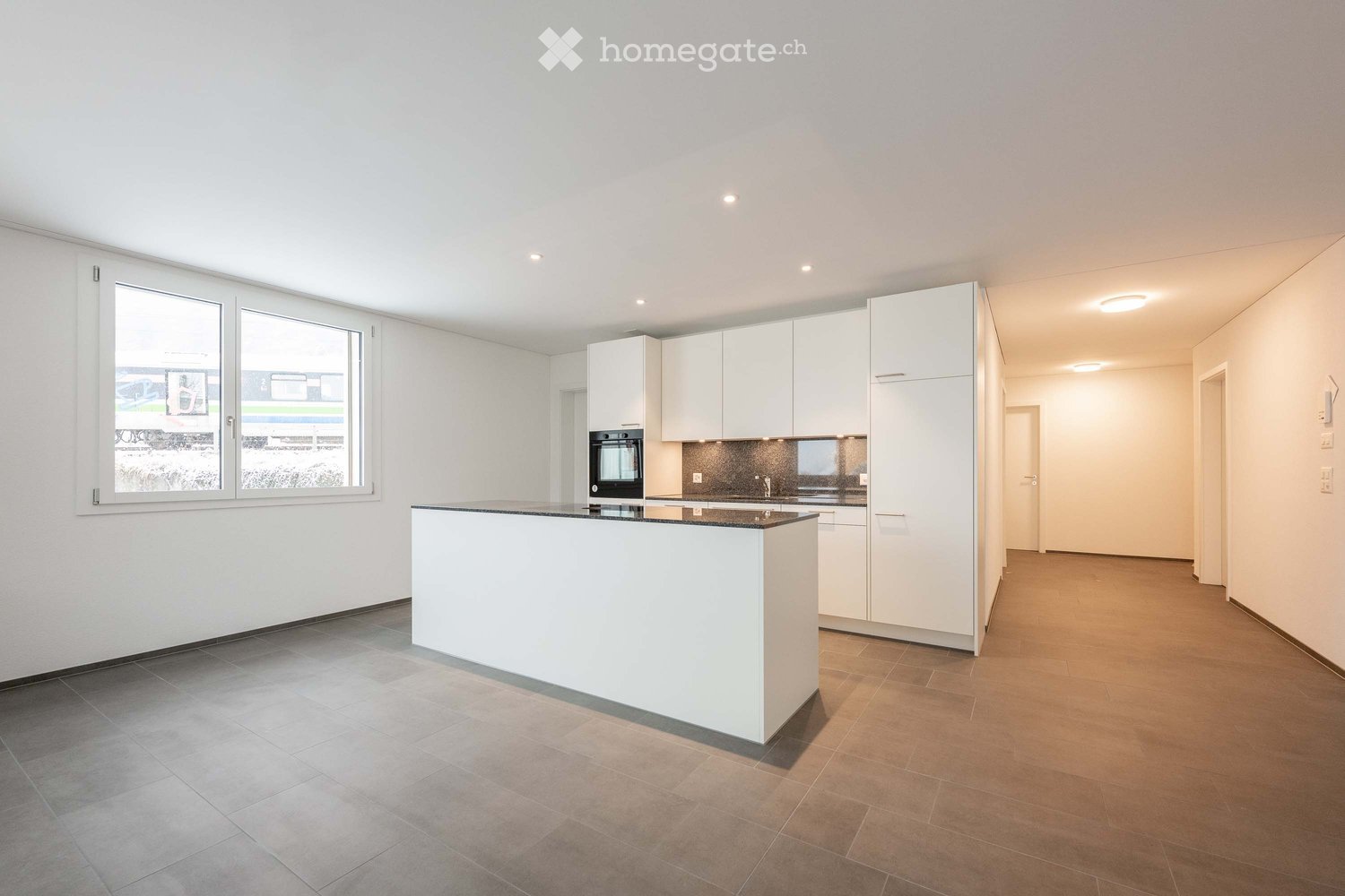 Modern kitchen with white cabinetry, a central island, and built-in appliances, featuring large windows and recessed lighting.