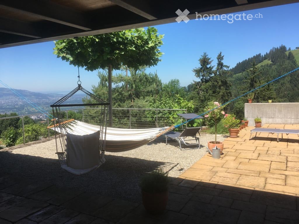 Outdoor patio with a hammock, lounge chairs, potted plants, and a scenic mountain view.