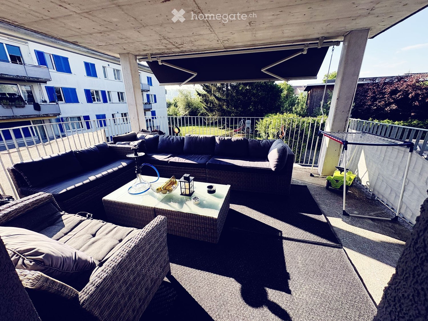 Balcony with a modern outdoor seating area featuring a sectional sofa, coffee table, and a small table with a hookah and fruit bowl.