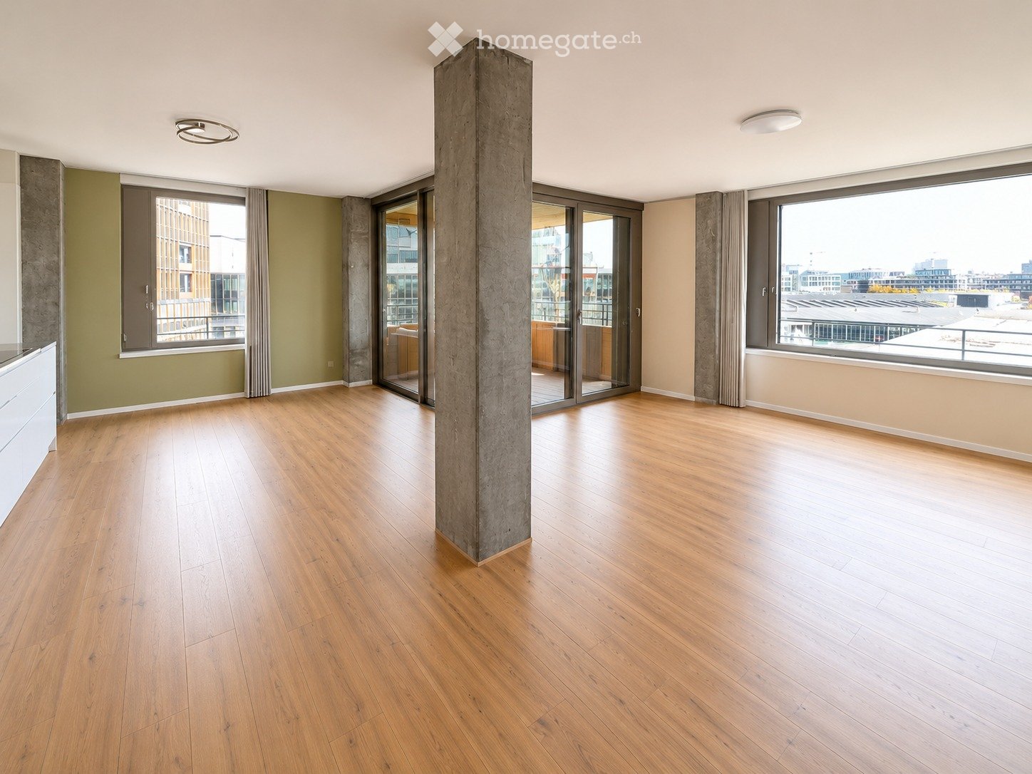 Empty room with wooden flooring, large windows, and a central concrete pillar. No furniture or equipment visible.