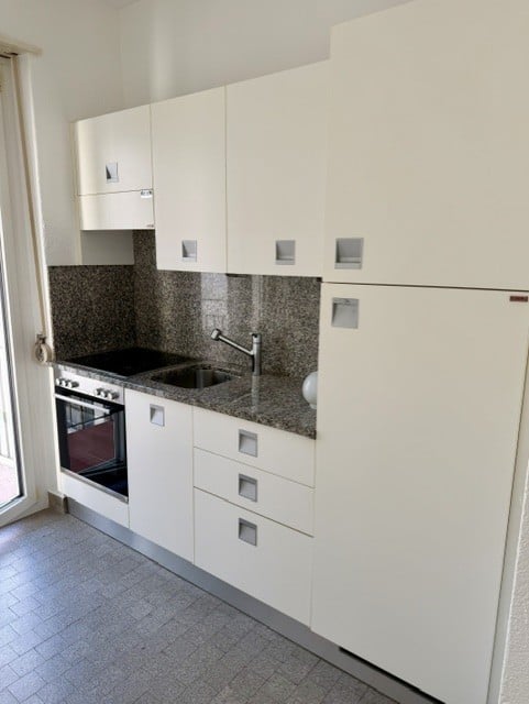 Modern kitchen with white cabinets, granite countertop, stainless steel sink and faucet, built-in oven, and refrigerator.