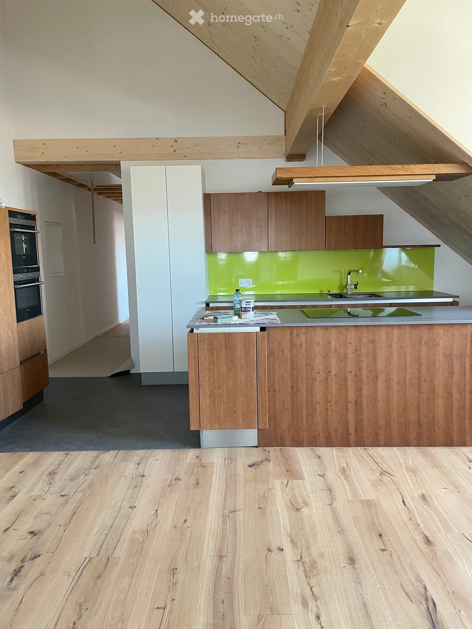 Modern kitchen with wooden cabinets, a central island, and a green backsplash. The space features a sleek design with a wooden floor and exposed wooden beams on the ceiling.