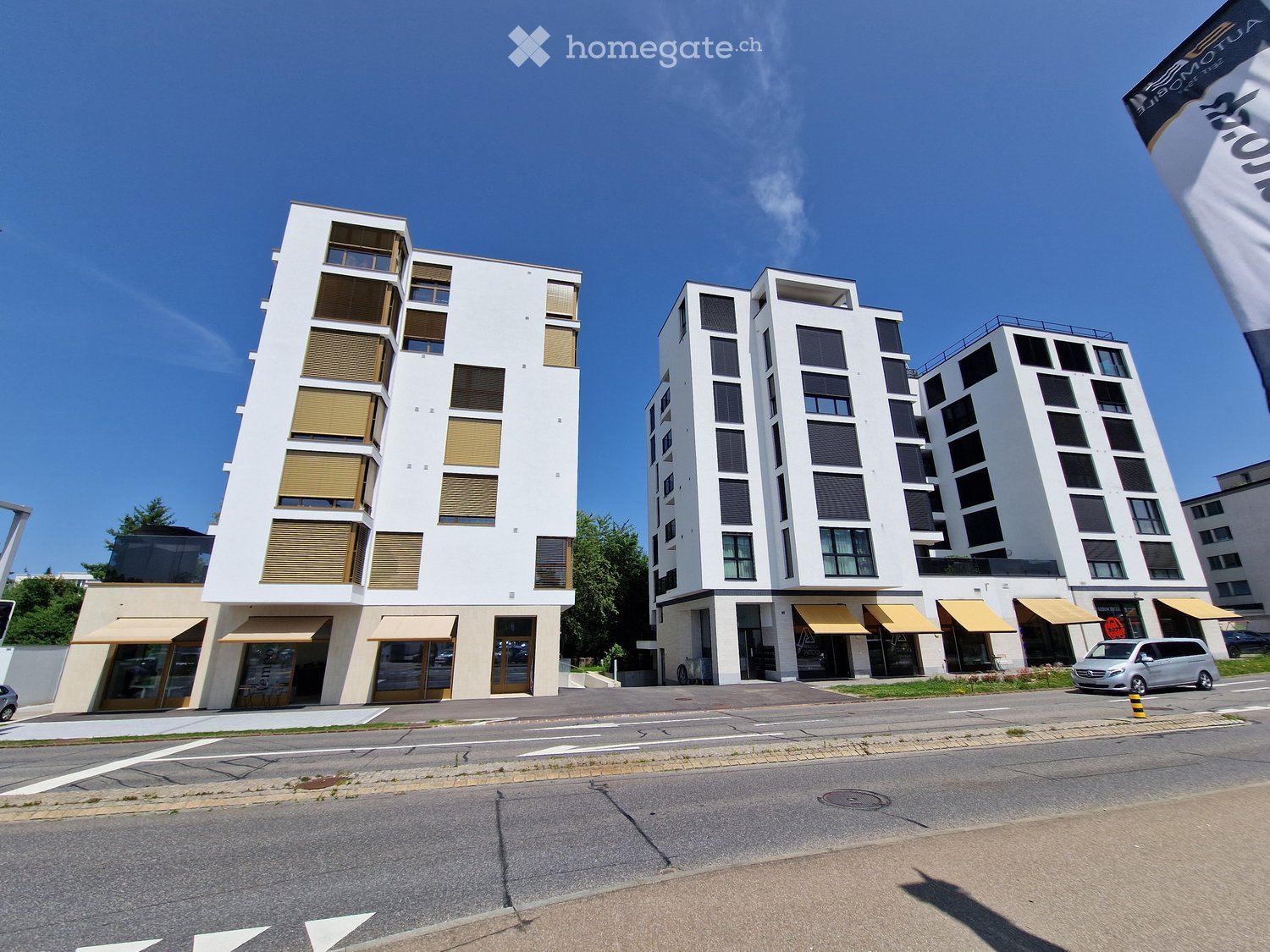 Modern multi-story residential building with white facade, large windows, and yellow awnings on the ground floor.