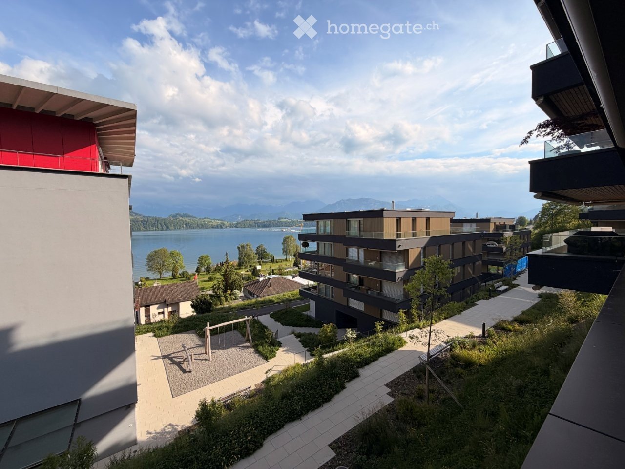 Modern residential complex with multiple buildings, balconies, and a scenic view of a lake and mountains in the background.