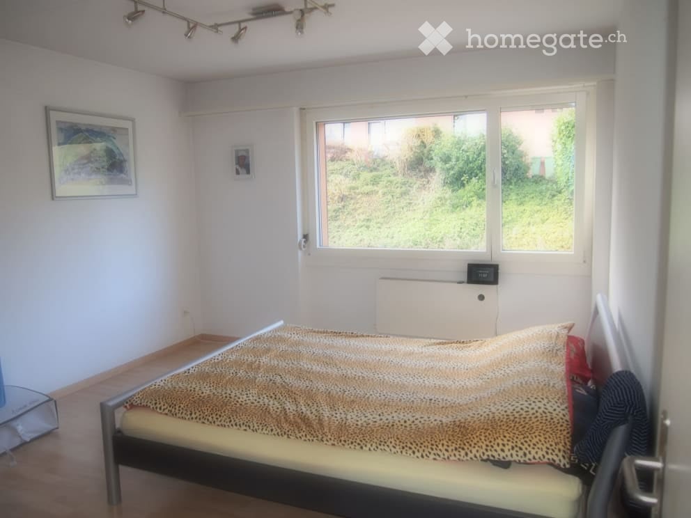 Bedroom with a single bed, leopard print bedspread, nightstand, picture frame, and a window with a view of greenery.