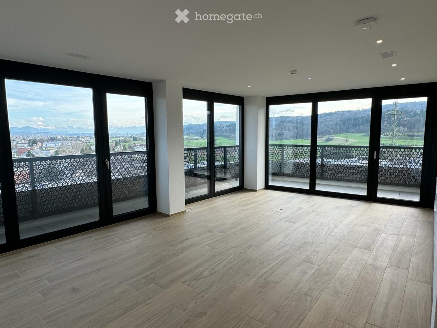 Empty room with wooden flooring and large sliding glass doors leading to a balcony with scenic mountain views.