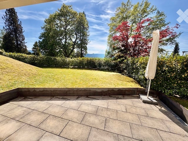Terraced outdoor area with tiled flooring, umbrella stand, and scenic view of trees and water.