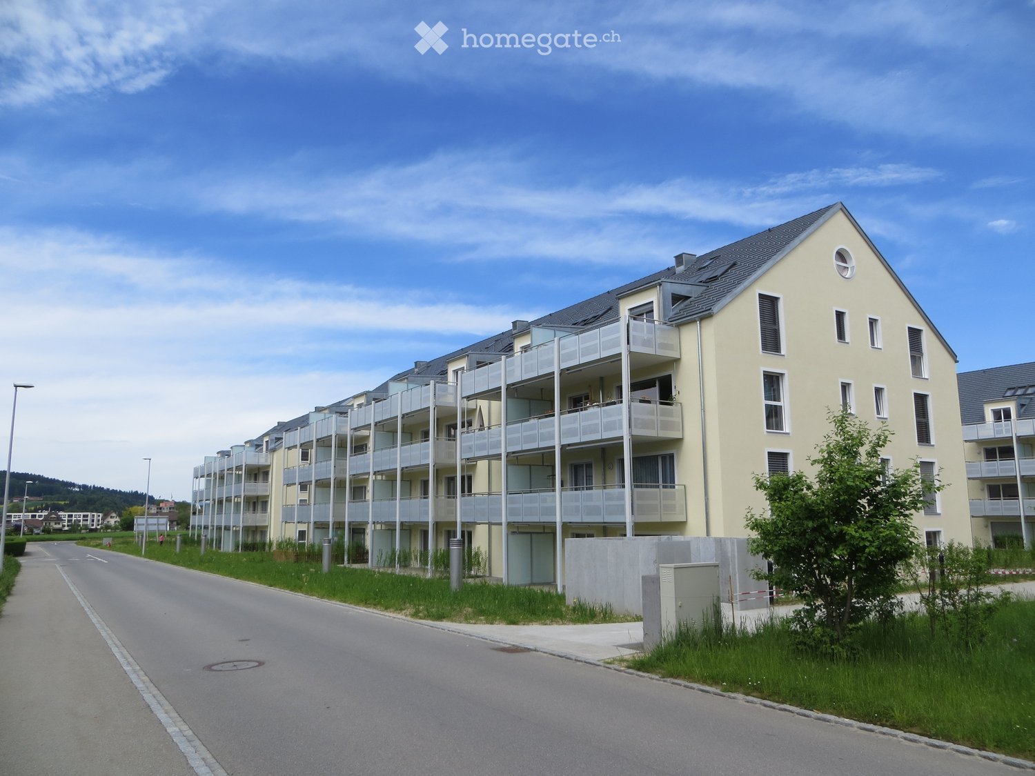 Modern multi-story residential building with balconies, light yellow facade, and grey roof.