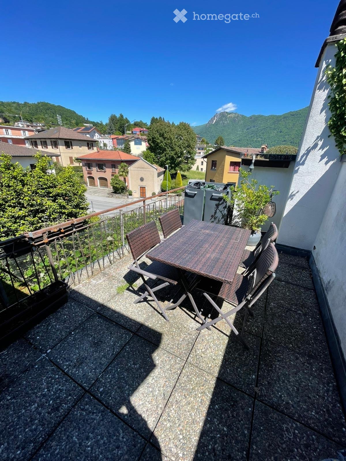 Balcony with a table and chairs, overlooking a scenic town and mountains.