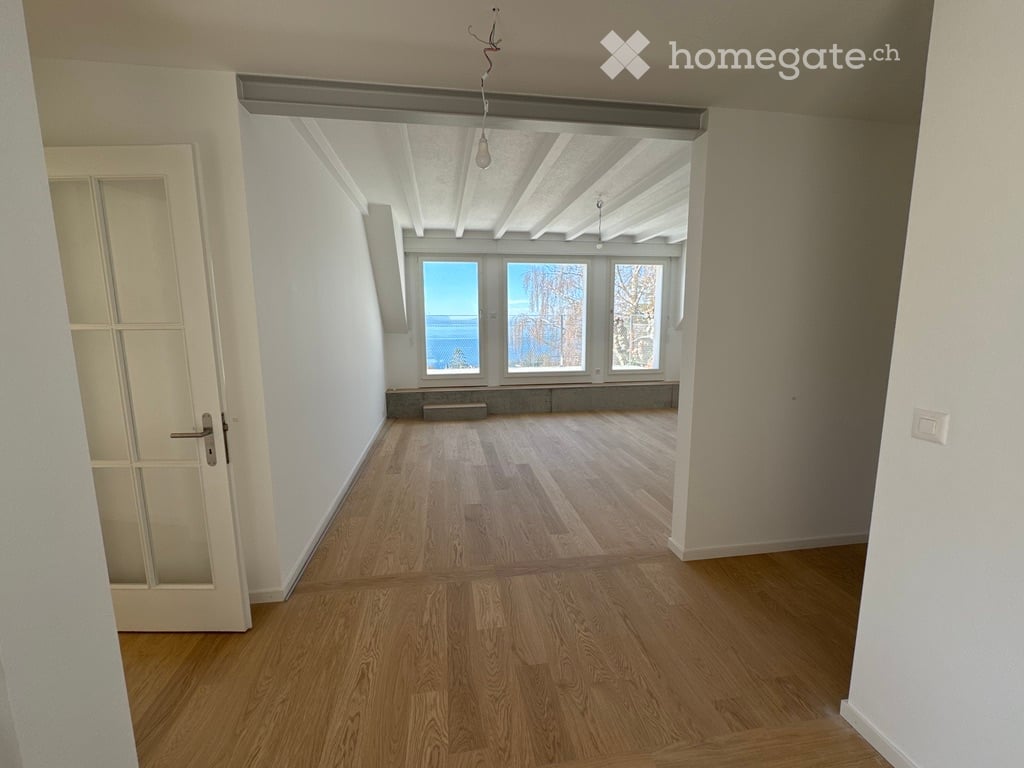 Empty room with wooden flooring, white walls, and large windows offering a view of the outdoors.