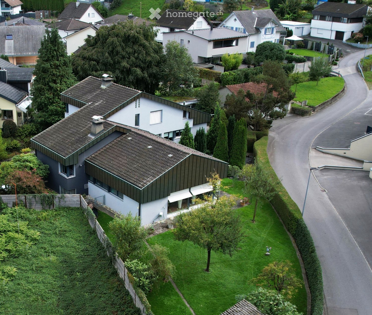 Aerial view of a residential neighborhood with multiple houses, well-maintained gardens, and a winding road.