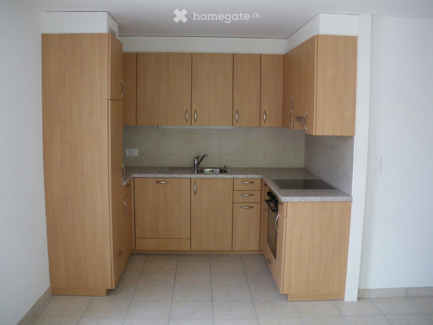 Modern kitchen with light wooden cabinets, a sink, a faucet, and an oven. The countertops are tiled, and the floor is tiled as well.