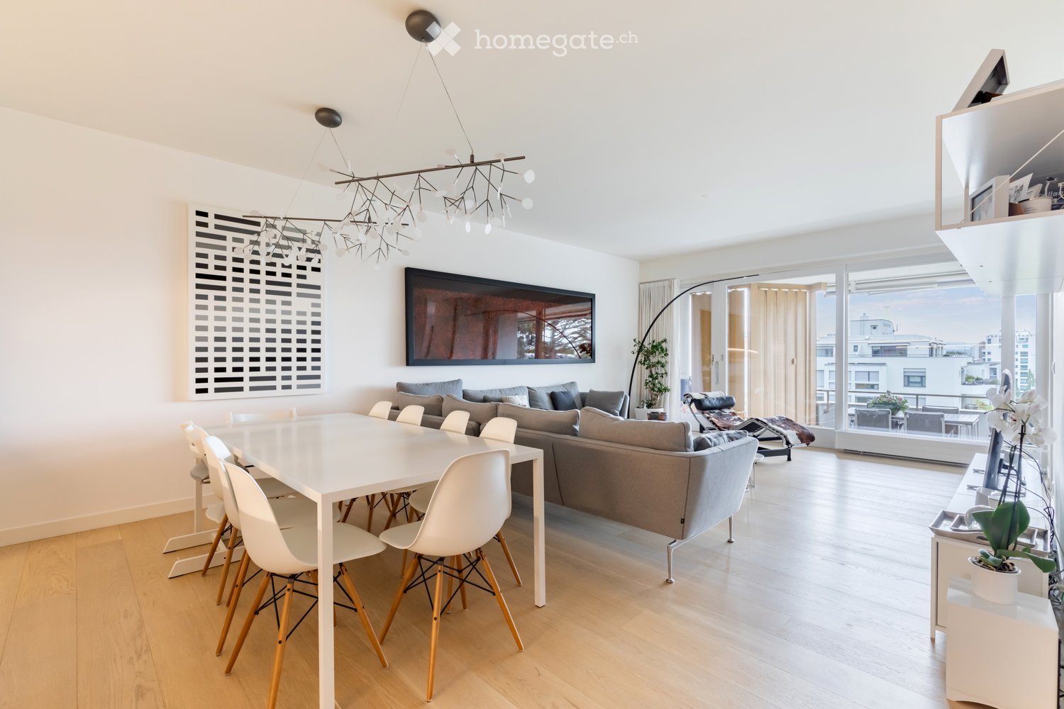 Dining table, modern grey couch, windows, floor lamp, wooden floor, chandelier