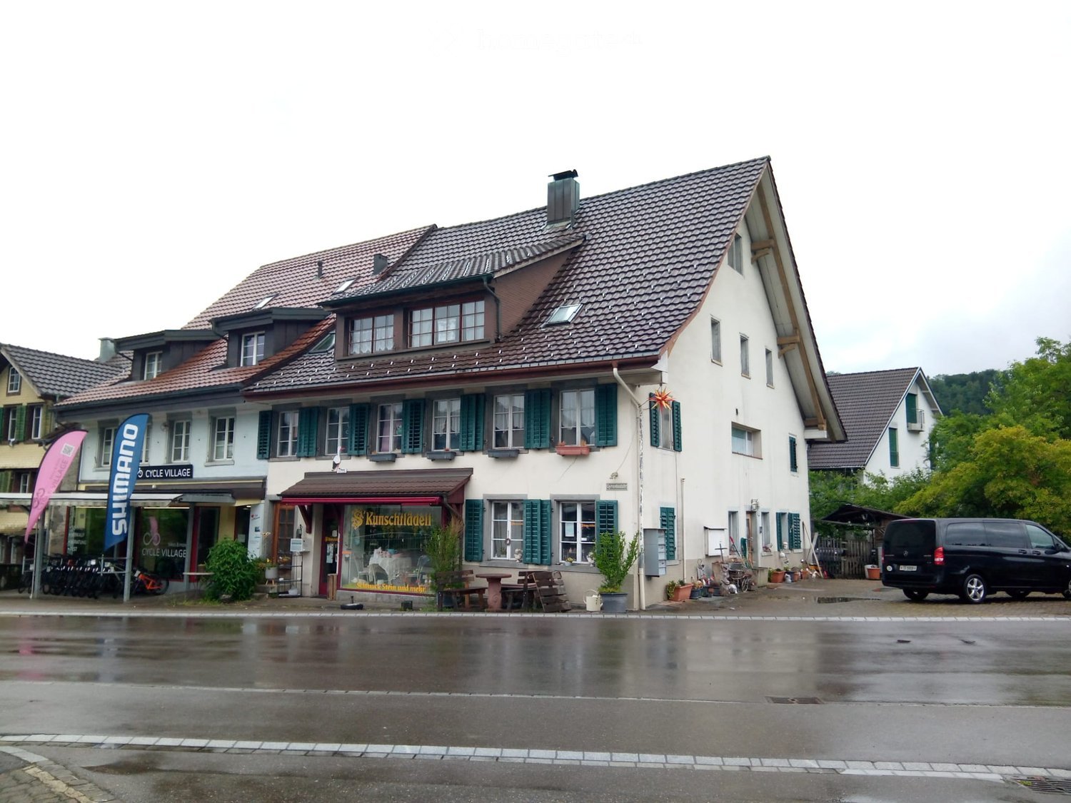 Two-story building with a red-tiled roof, multiple windows with shutters, and a storefront with a sign reading "Kunstschdeli".