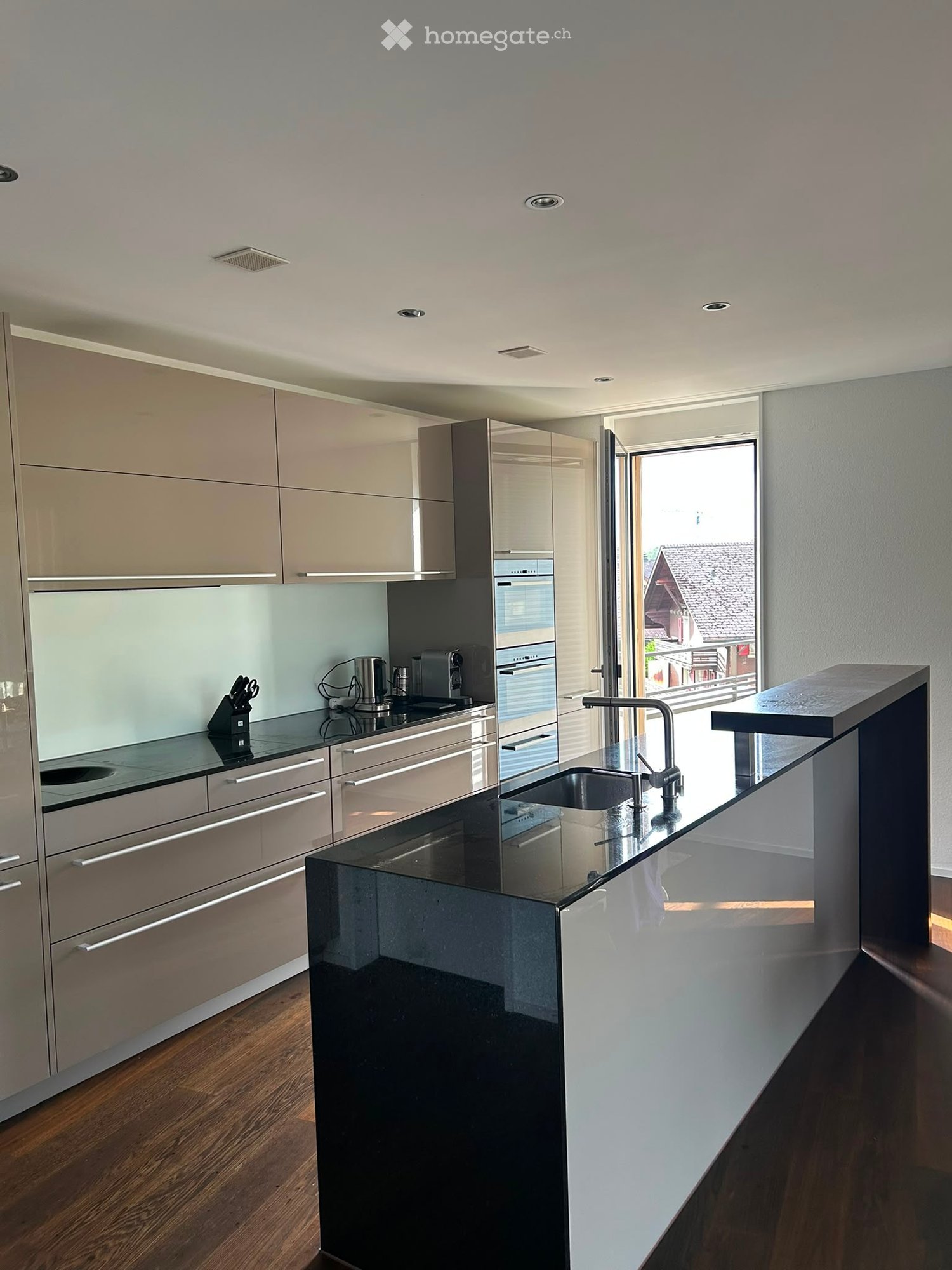 Modern kitchen with light-colored cabinets, black countertops, stainless steel appliances, and a large island with a sink and faucet.