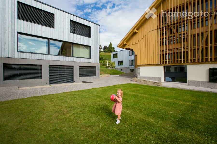A well-maintained lawn in front of modern residential buildings, with a child playing with a ball.