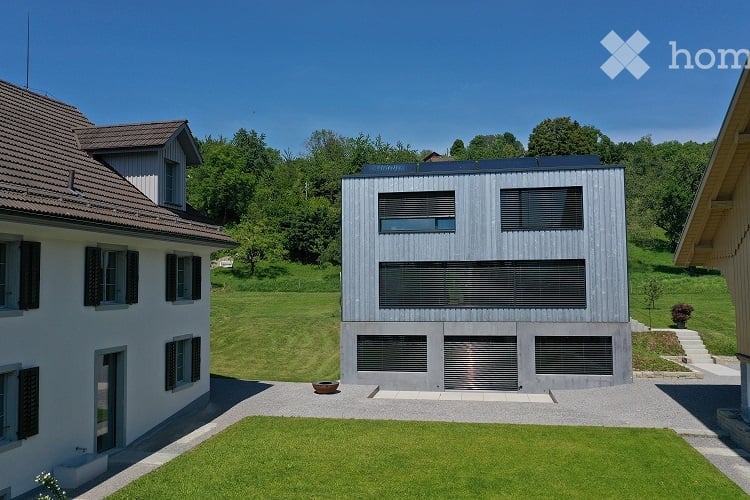 Modern two-story building with a flat roof and large windows, surrounded by a well-maintained lawn and trees.