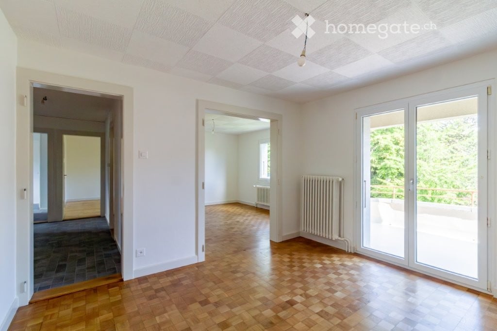 Empty room with wooden flooring, white walls, large sliding glass doors leading to a balcony, and visible radiators.