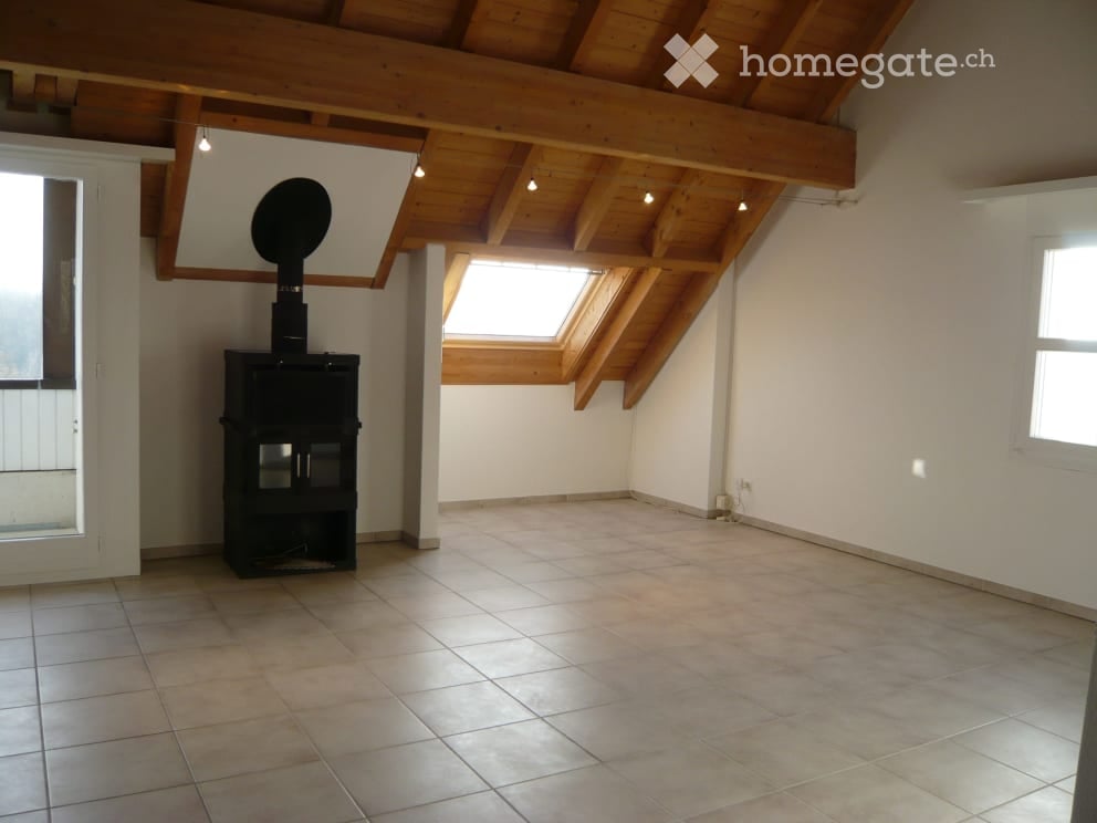 Empty room with exposed wooden beams, tiled floor, and a black wood-burning stove. Skylight windows allow natural light.