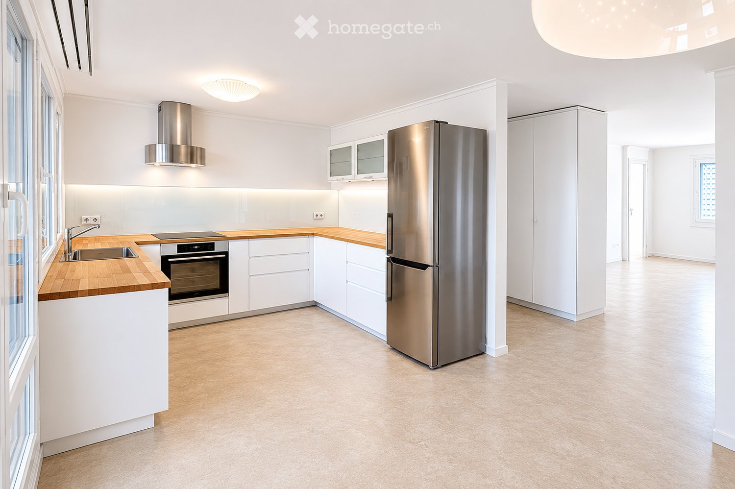Modern kitchen with white cabinets, wooden countertops, stainless steel appliances, and a large window.