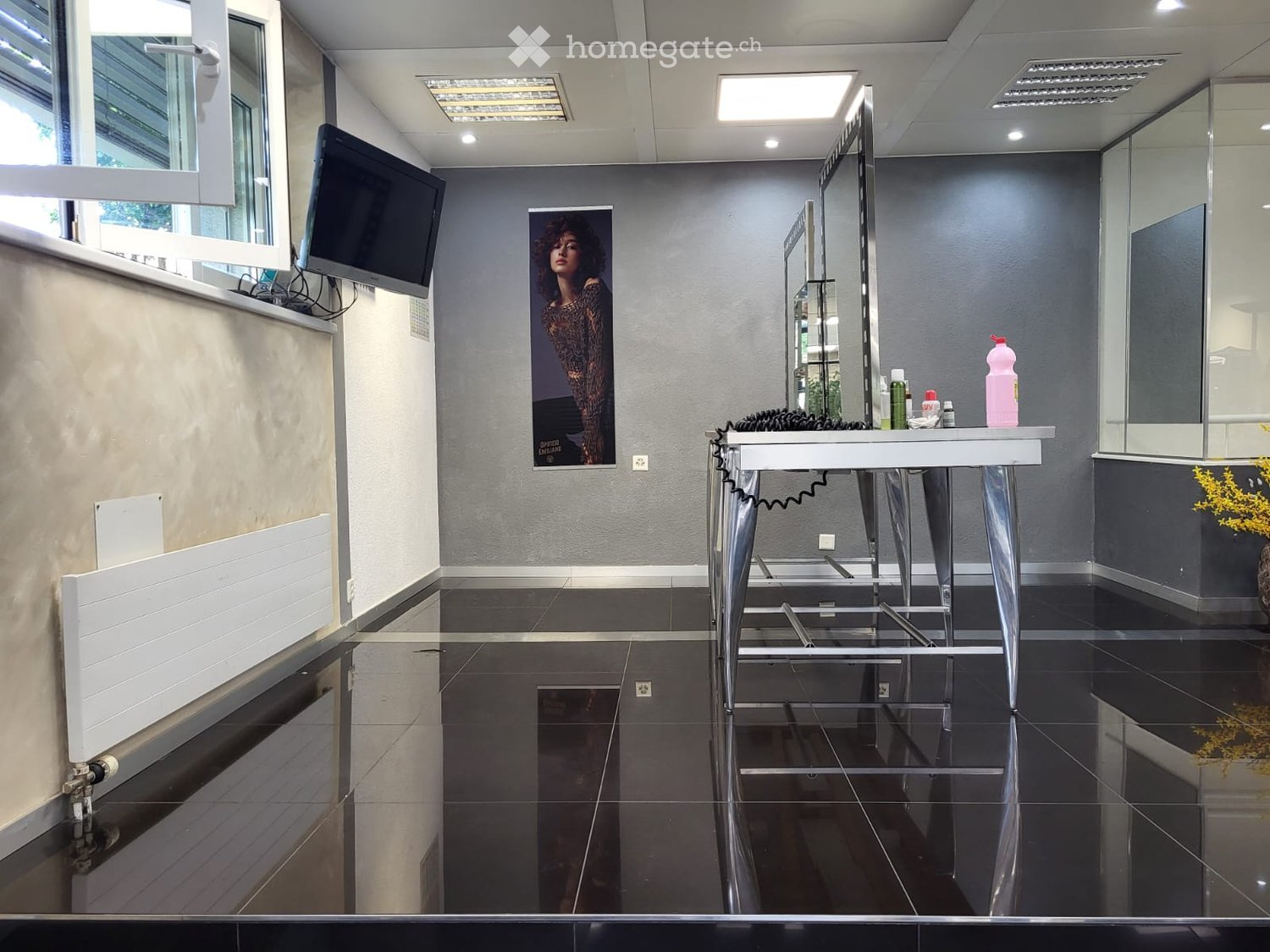 Modern, sleek room with a large mirror, a small table holding bottles, a screen mounted on the wall, and a stylish poster.