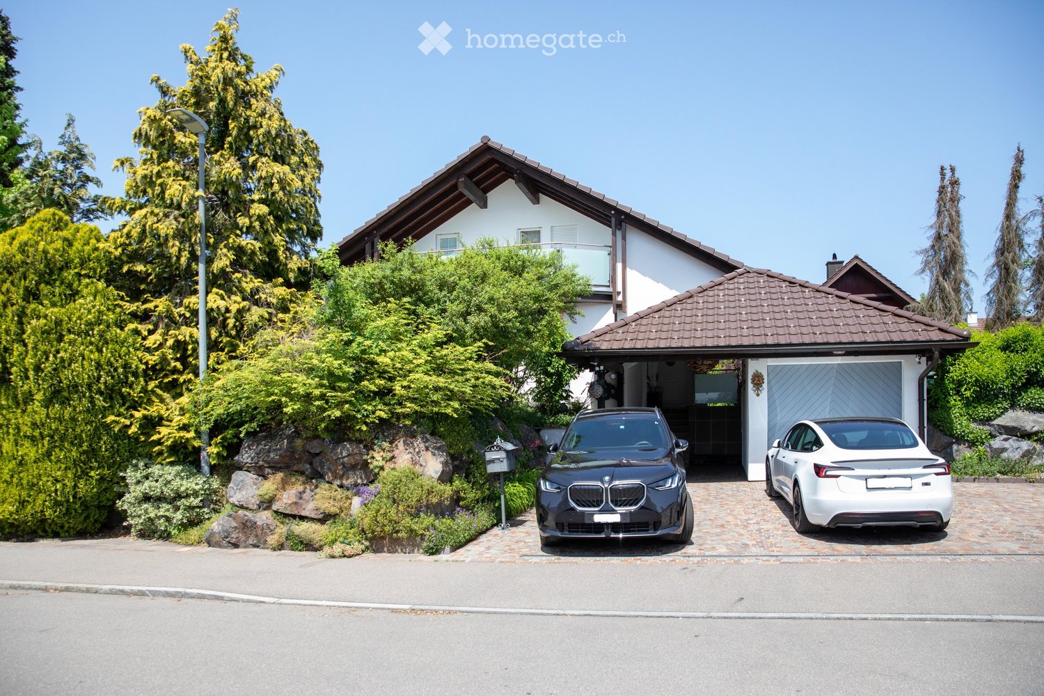 Two-story house with a garage, two parked cars, and well-maintained landscaping.